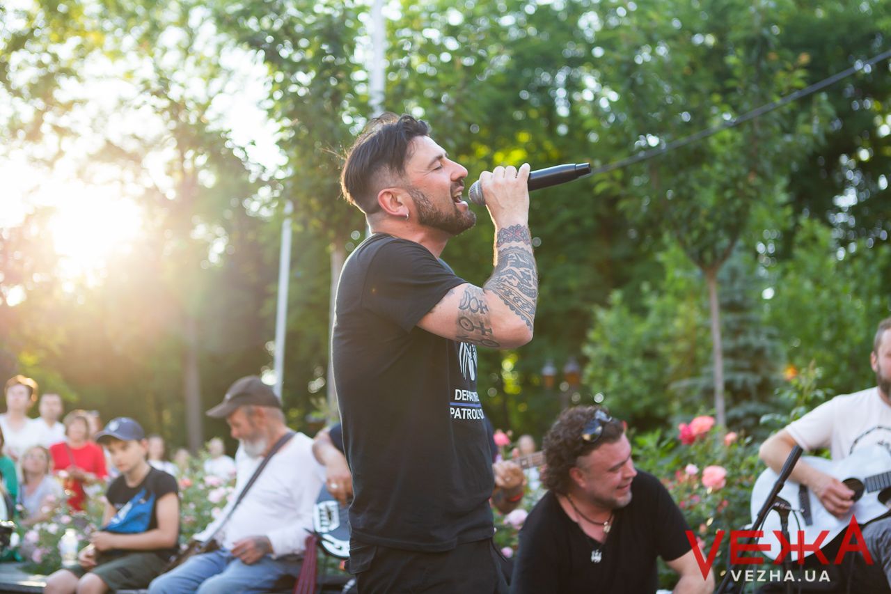 Singer performing at sunset during outdoor concert with trees in background.