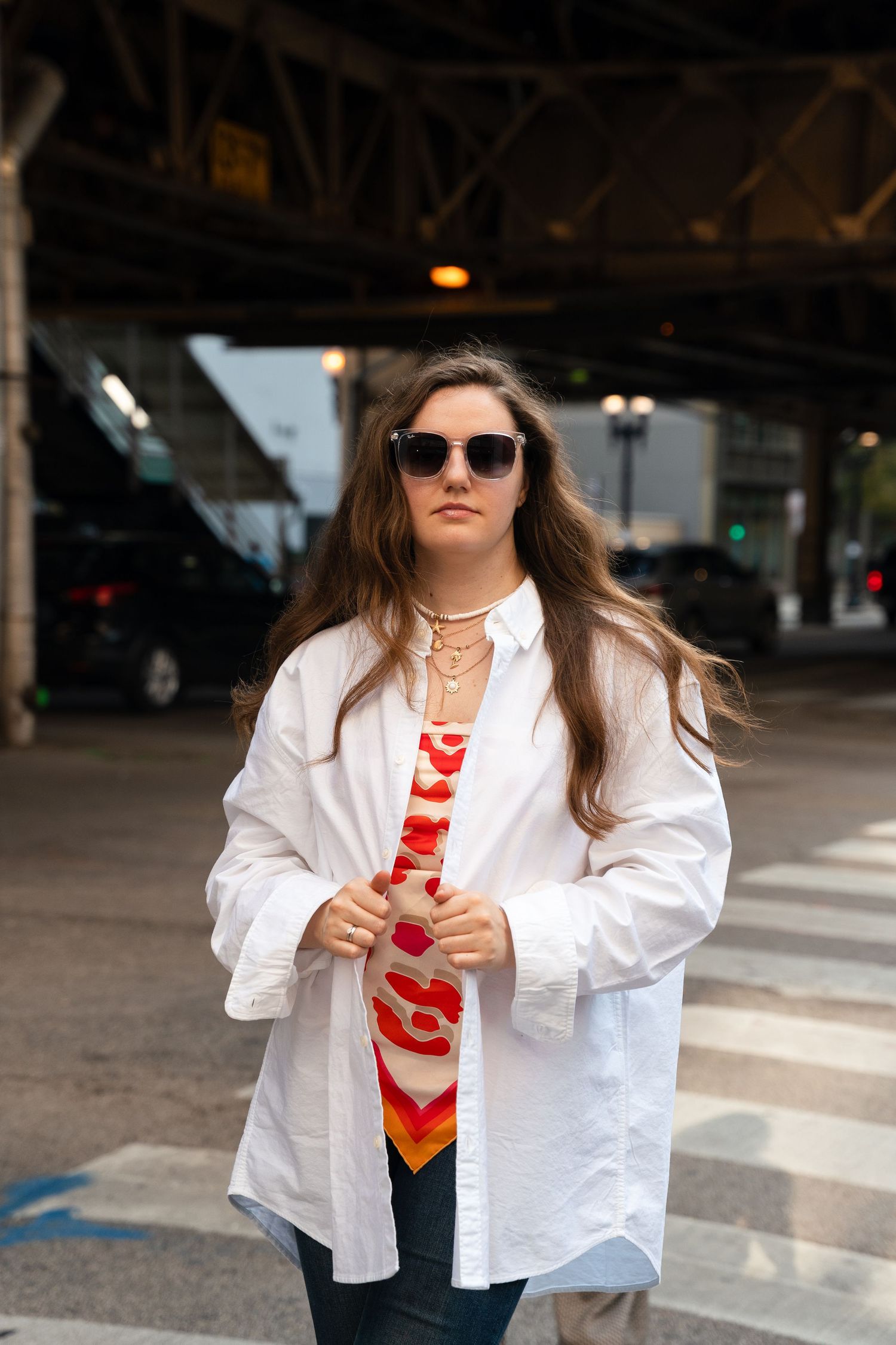 Street style photo under bridge wearing oversized white shirt and sunglasses in urban setting.