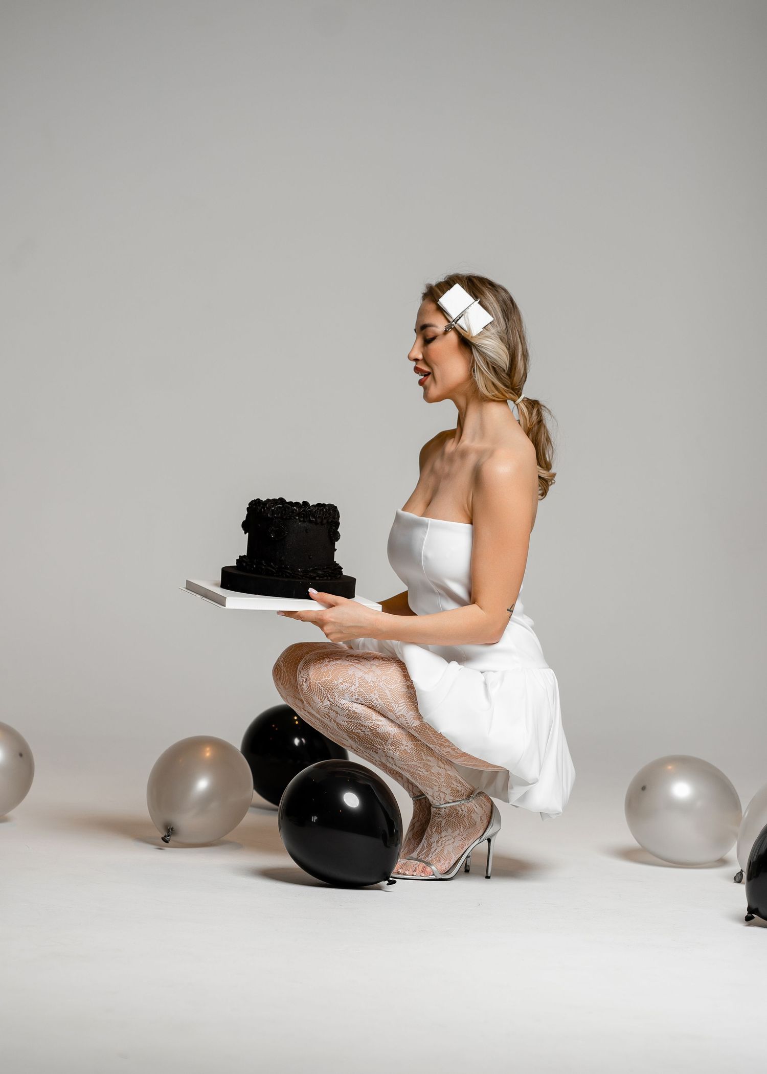 A series of four minimalist studio photos showing someone in a white dress crouching beside black and white balloons.
