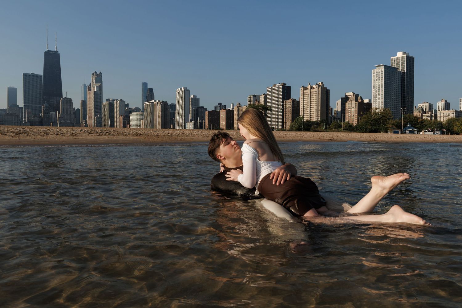 People enjoy swimming in Lake Michigan with the Chicago skyline visible in the background on a sunny day.