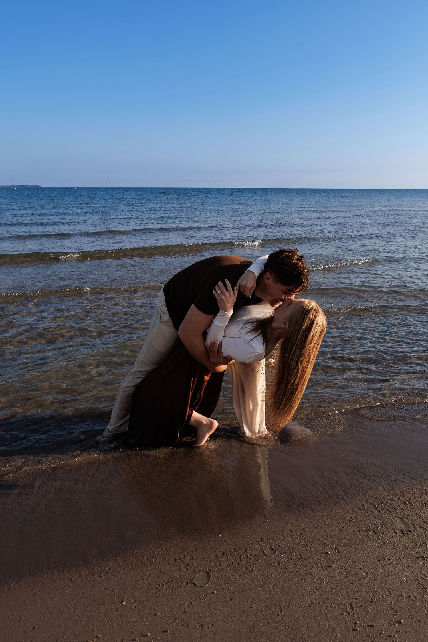 A couple shares a romantic moment on the beach at sunset as waves lap at the shore.