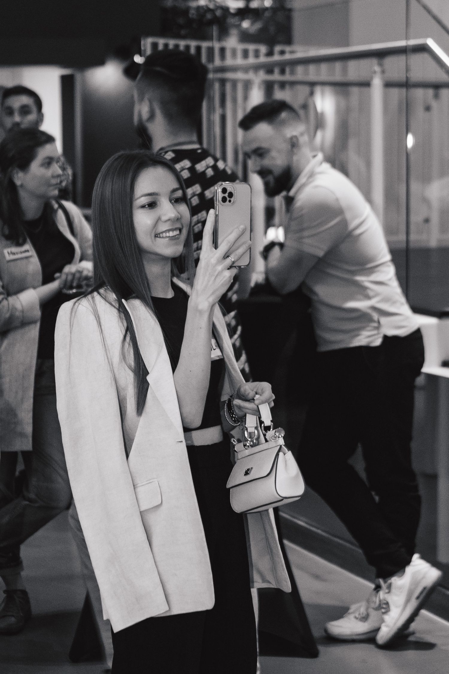 Person taking a photo on their phone at an indoor event wearing a white blazer and dark outfit.