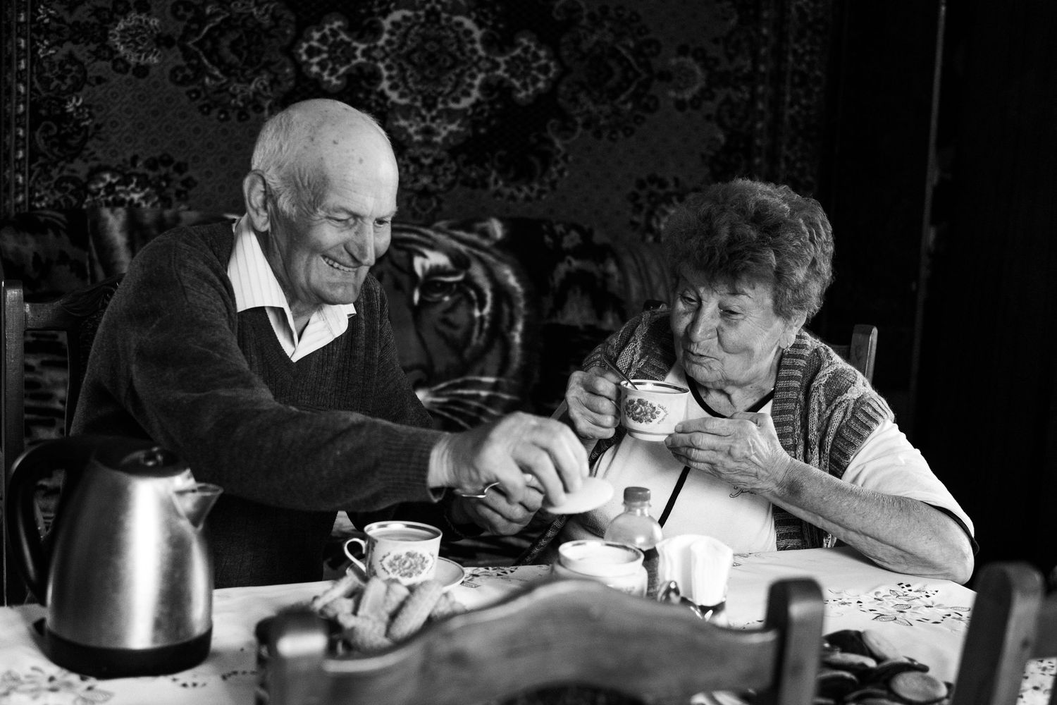 Black and white photo of two people having tea at a table.