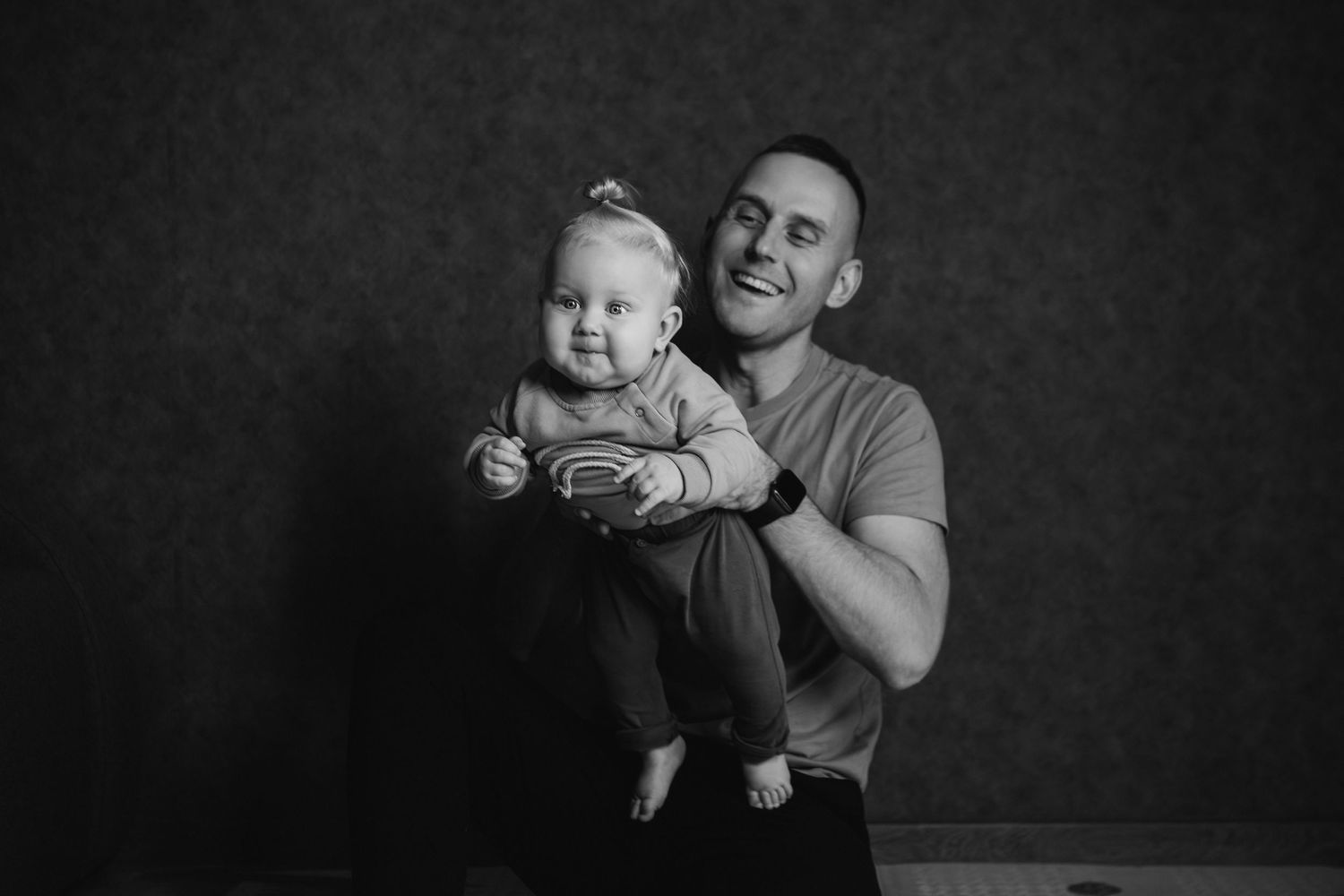 Black and white studio portrait of an adult and baby against a dark background.