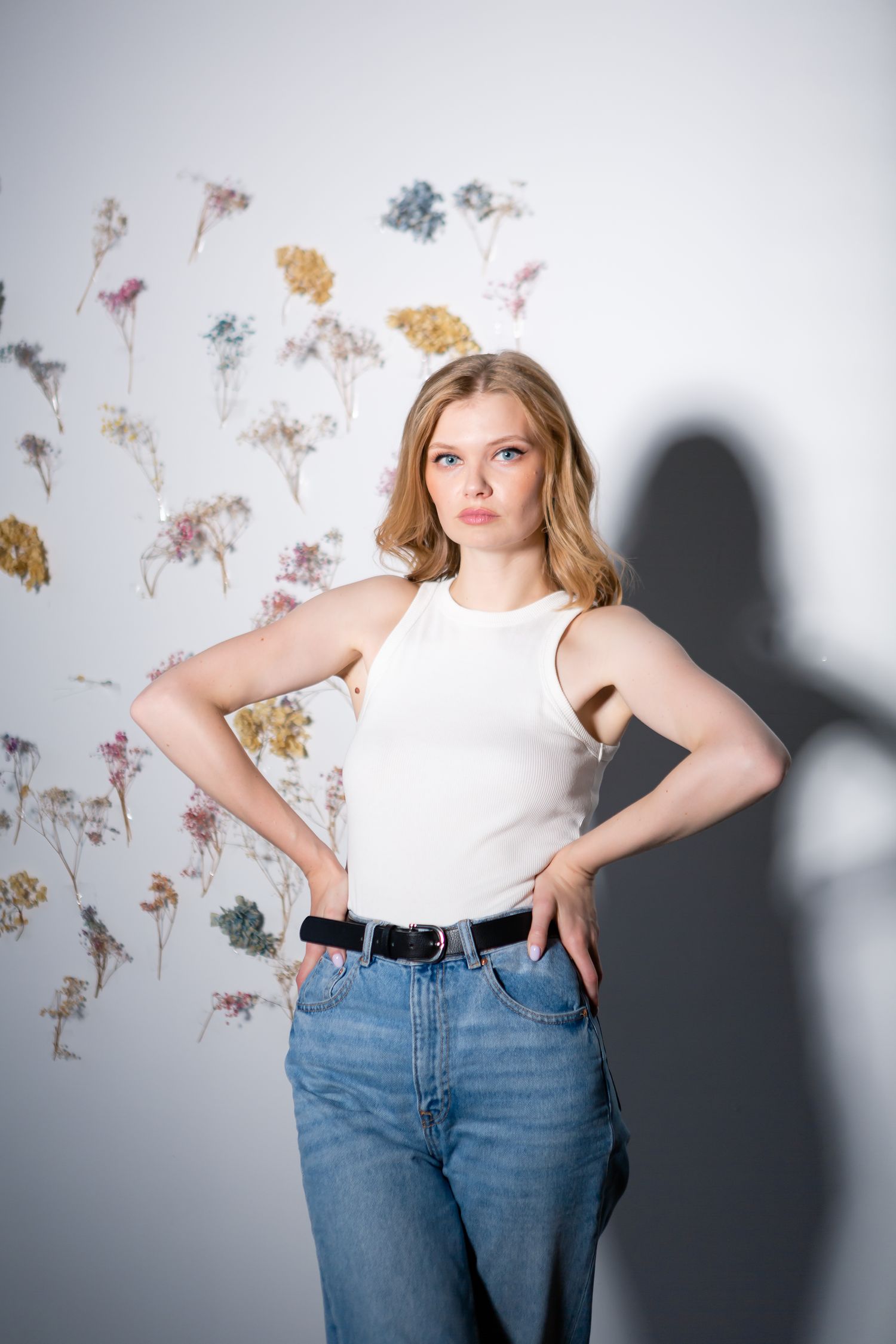 Casual portrait with pressed flower wall art featuring white tank top and classic denim look.