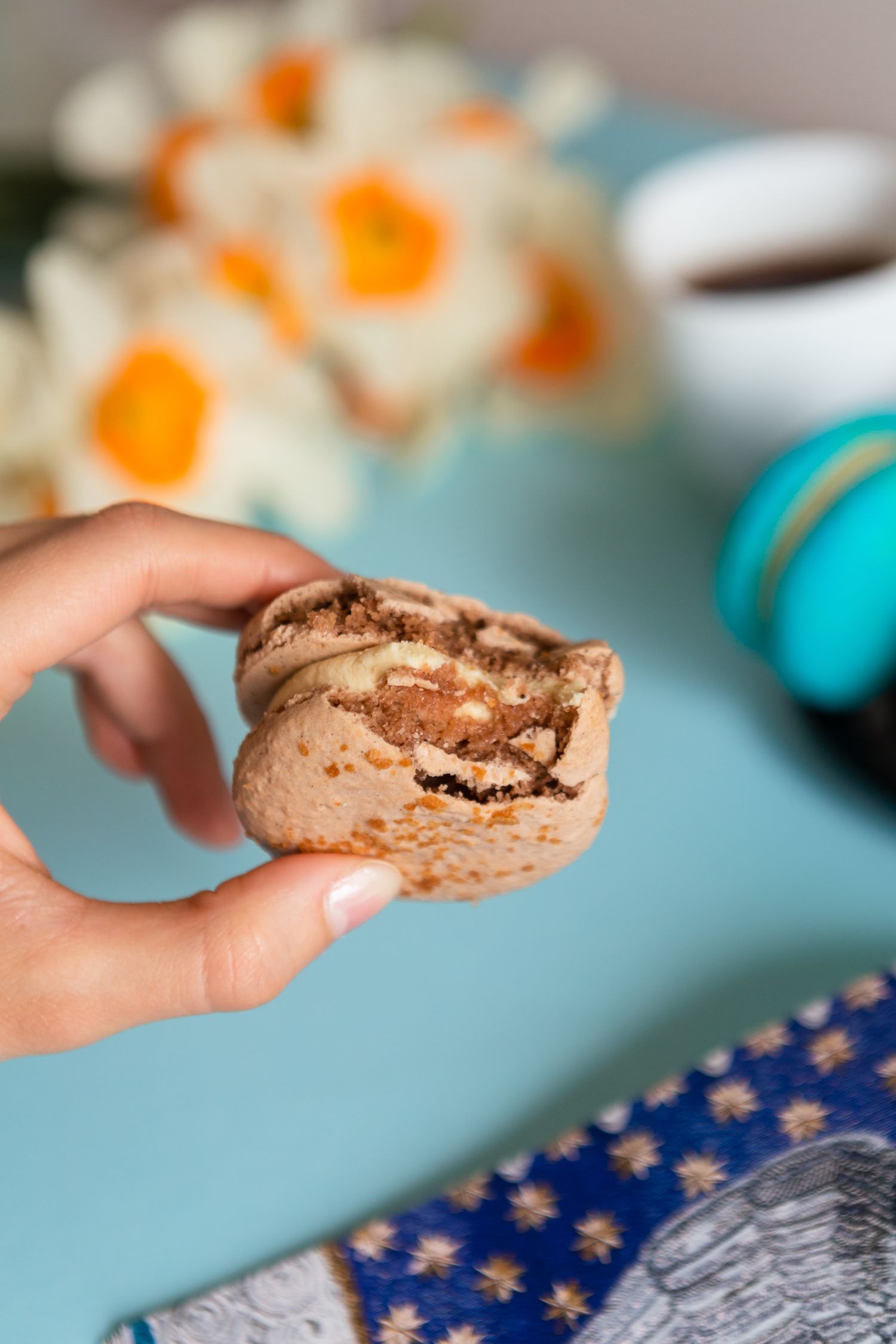 Close up view of a chocolate macaron being held up to show the filling texture.