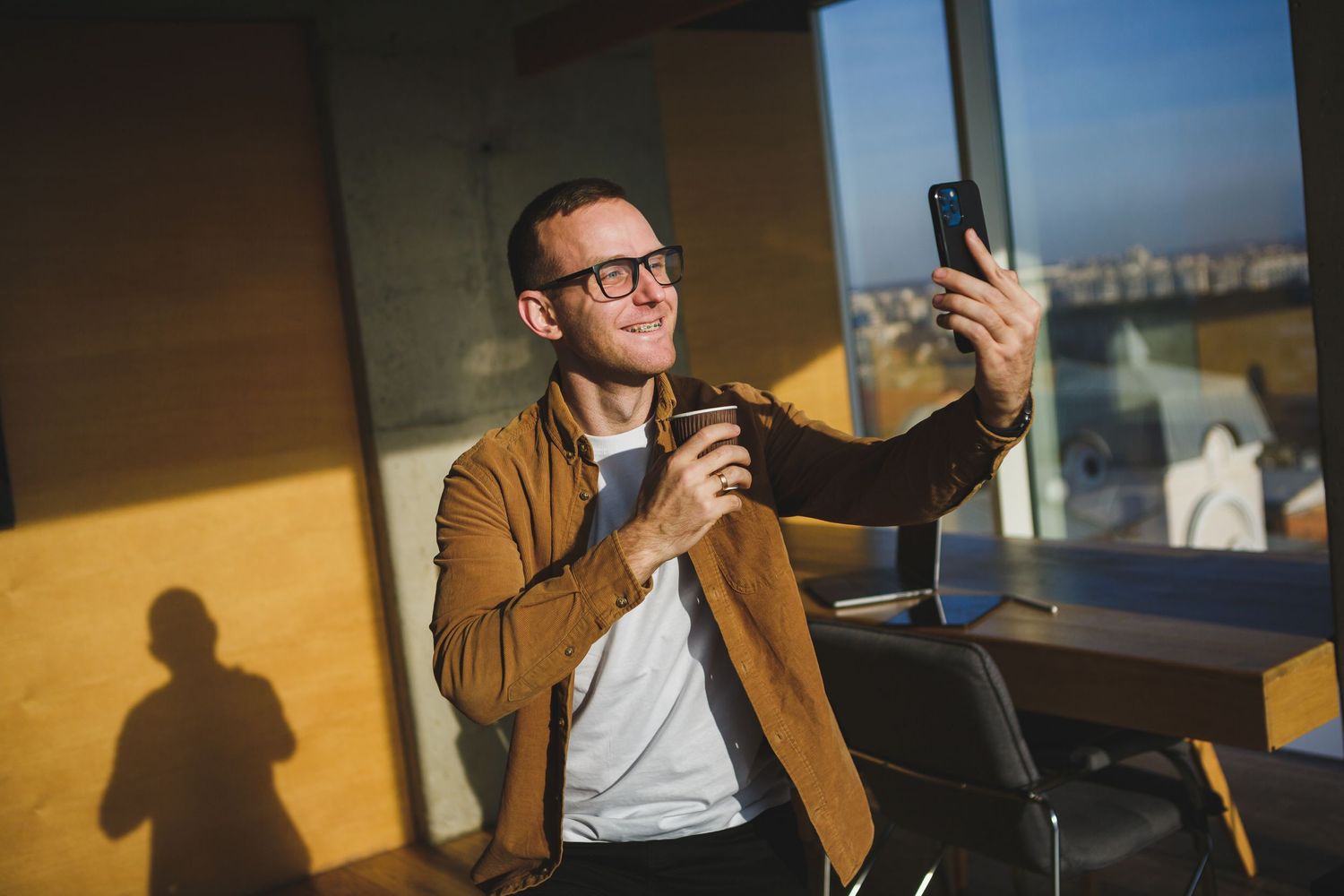 Business professional taking selfie in modern office with city view.