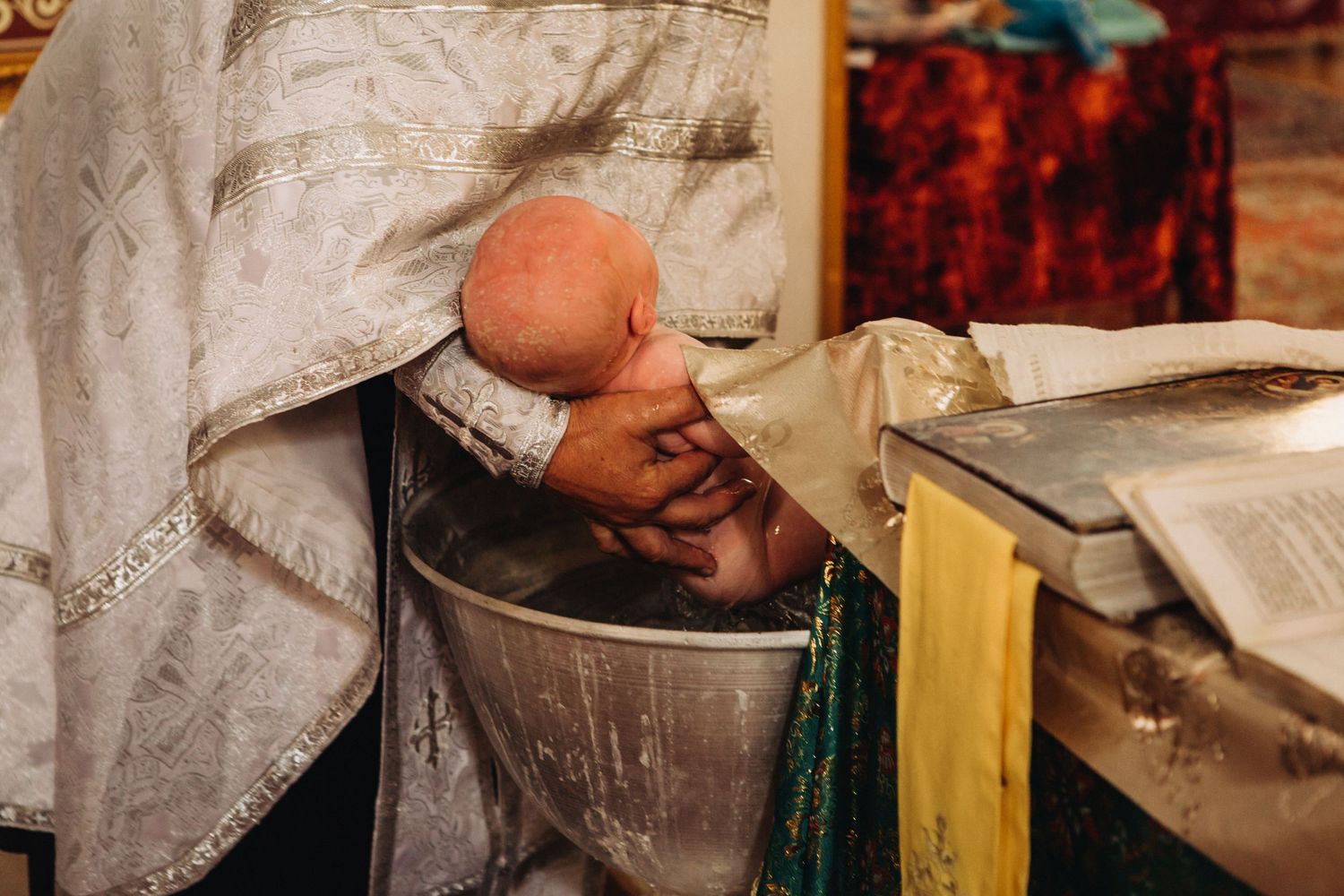 Orthodox baptism ritual showing immersion in traditional baptismal font.