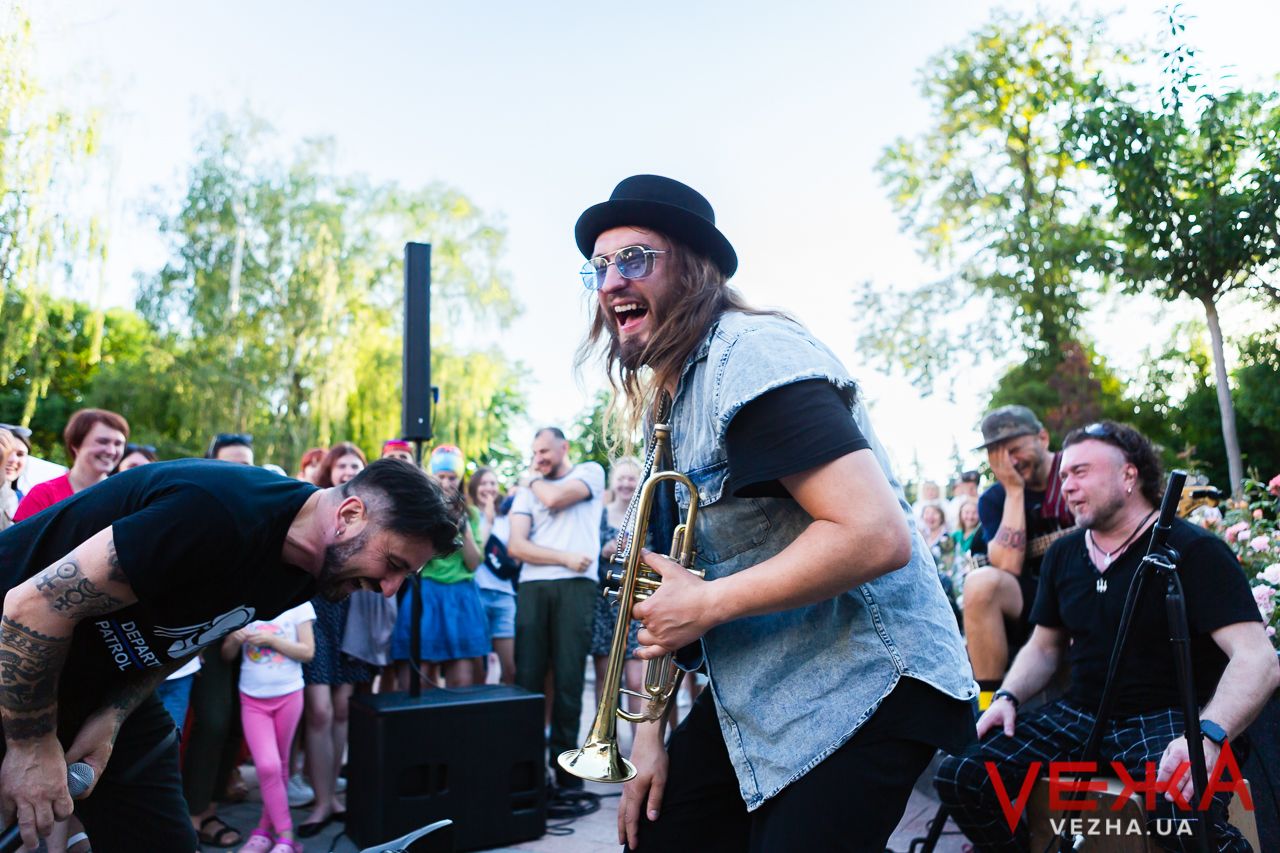 Musicians energetically performing on outdoor stage with animated expressions.