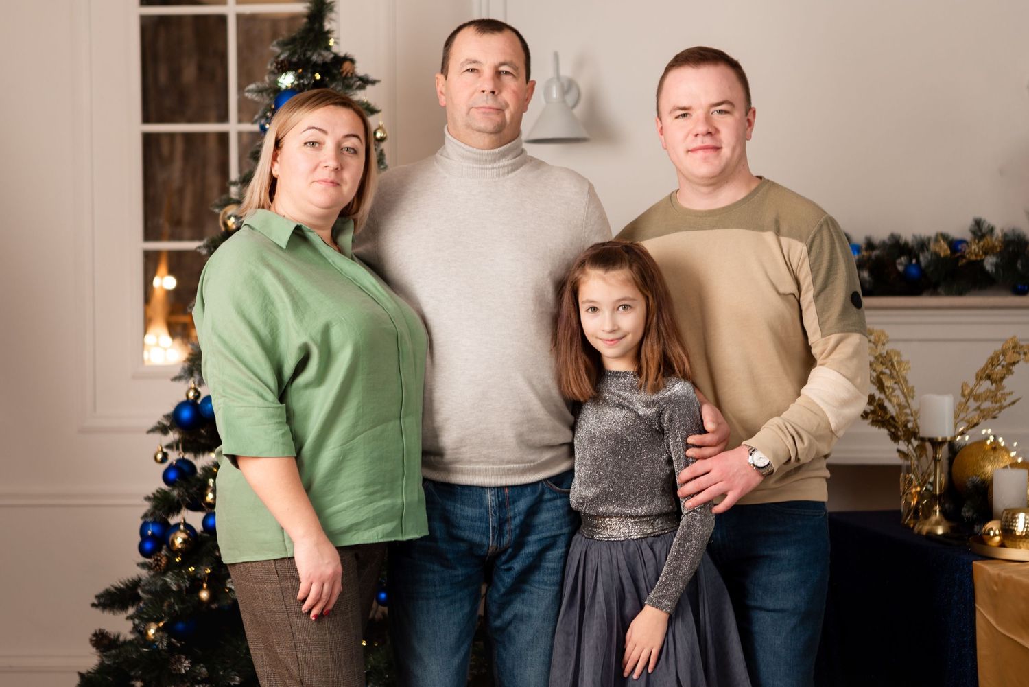 Family group poses in casual attire in front of Christmas tree and holiday decorations.