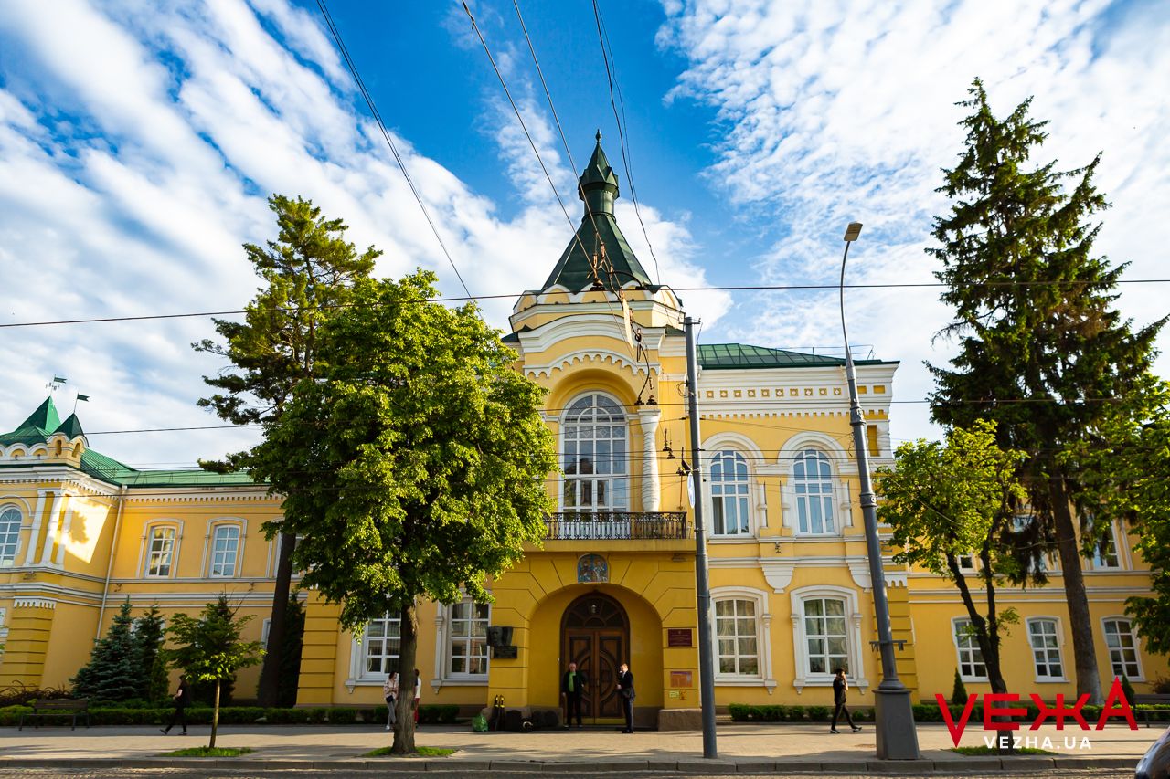 Yellow classical building with ornate architecture and green dome under dramatic blue sky.