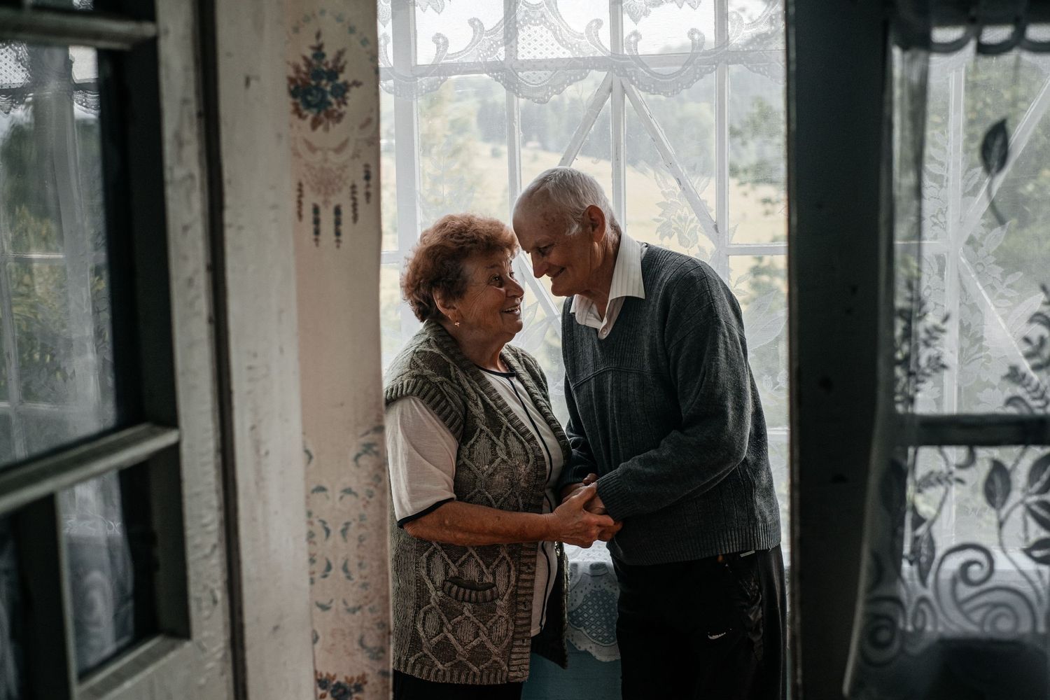 Tender moment shared between two people by a window with lace curtains.