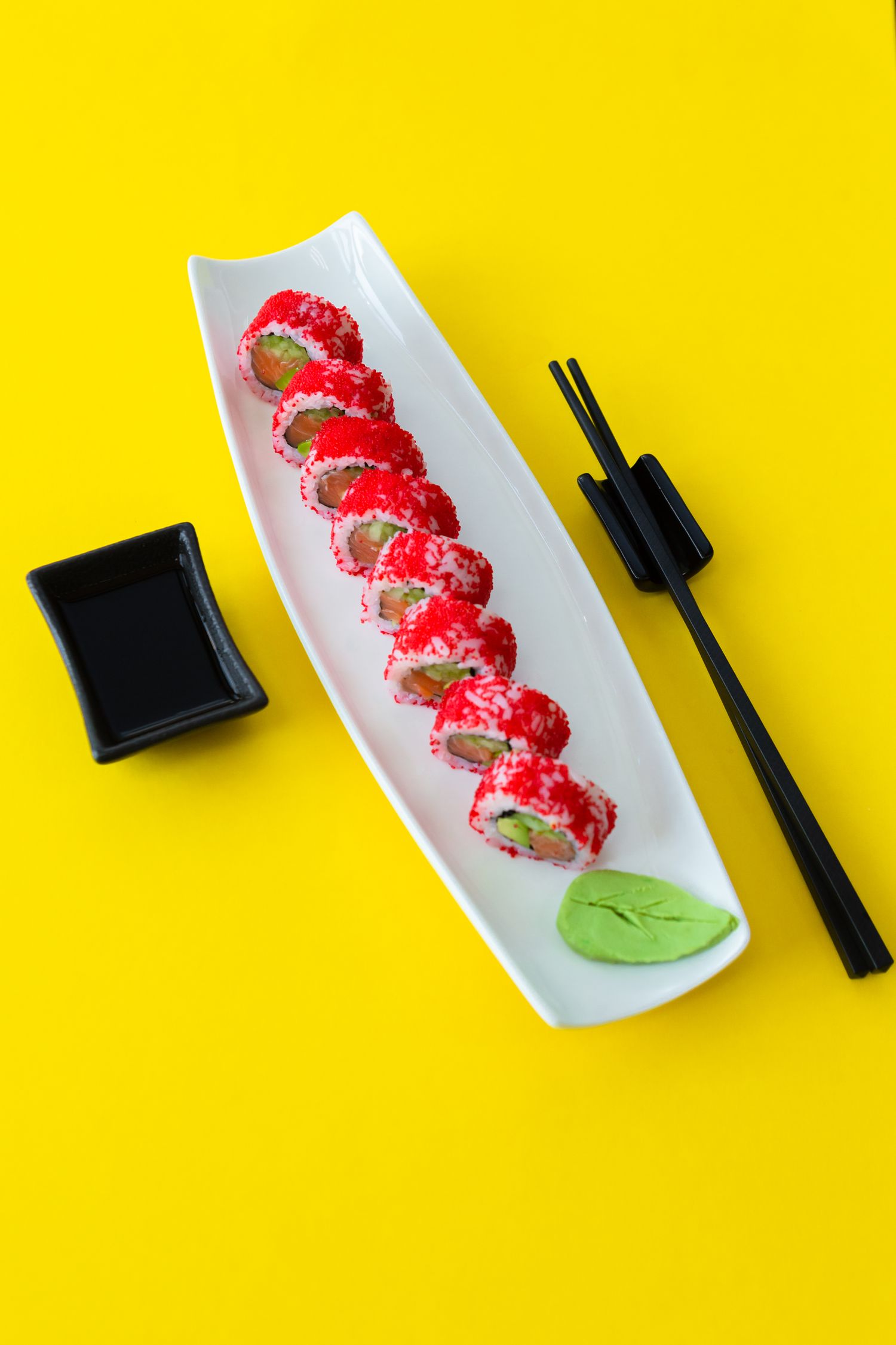 Fresh sushi roll with strawberries plated on white dish with chopsticks and soy sauce.