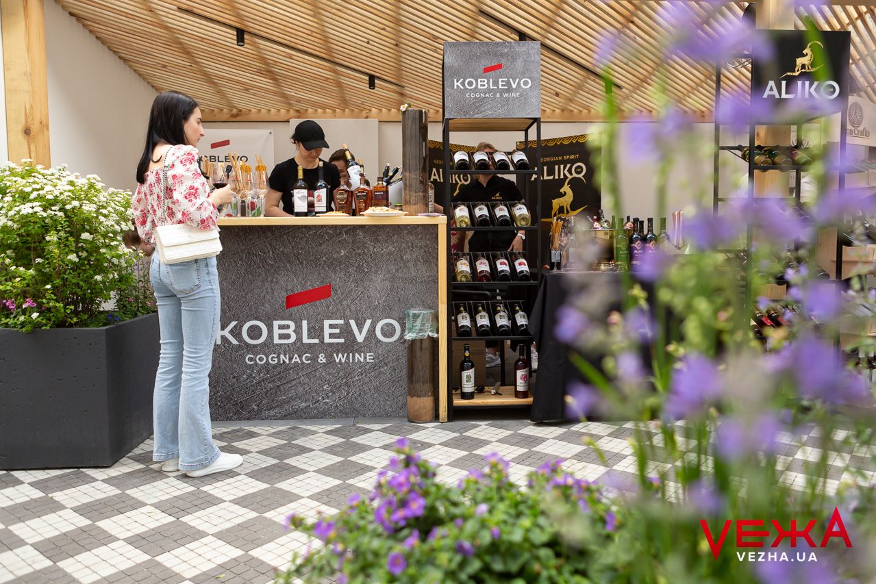 Outdoor wine tasting counter with wooden roof and purple flowers in foreground.