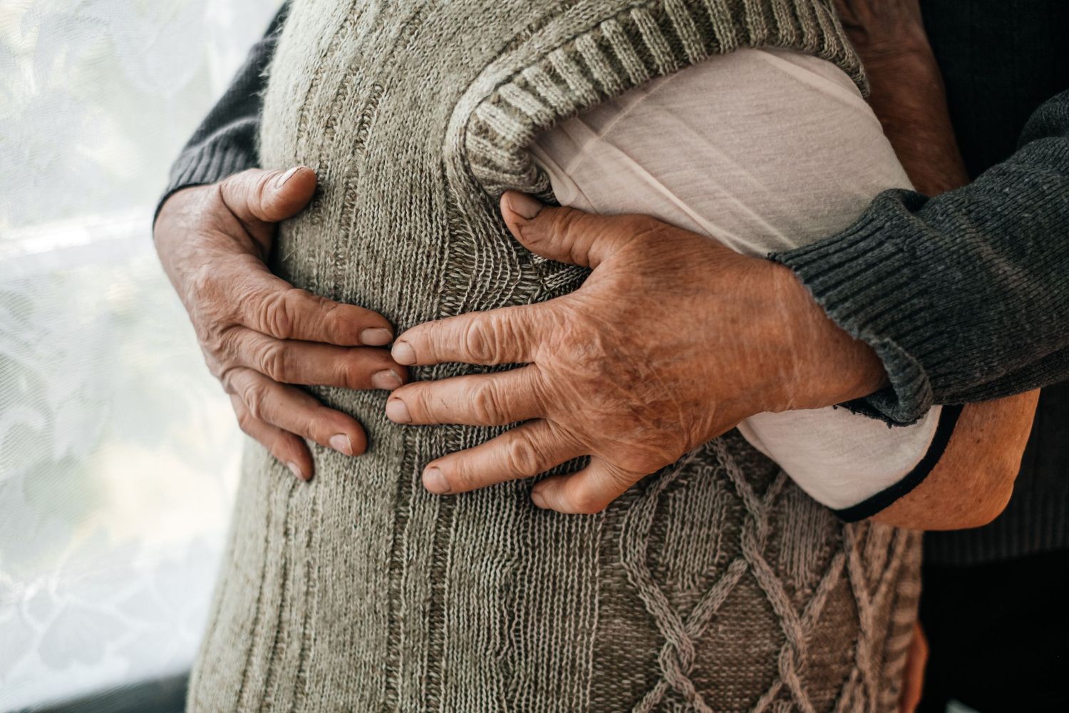 Weathered hands clasped together over a gray knit sweater.