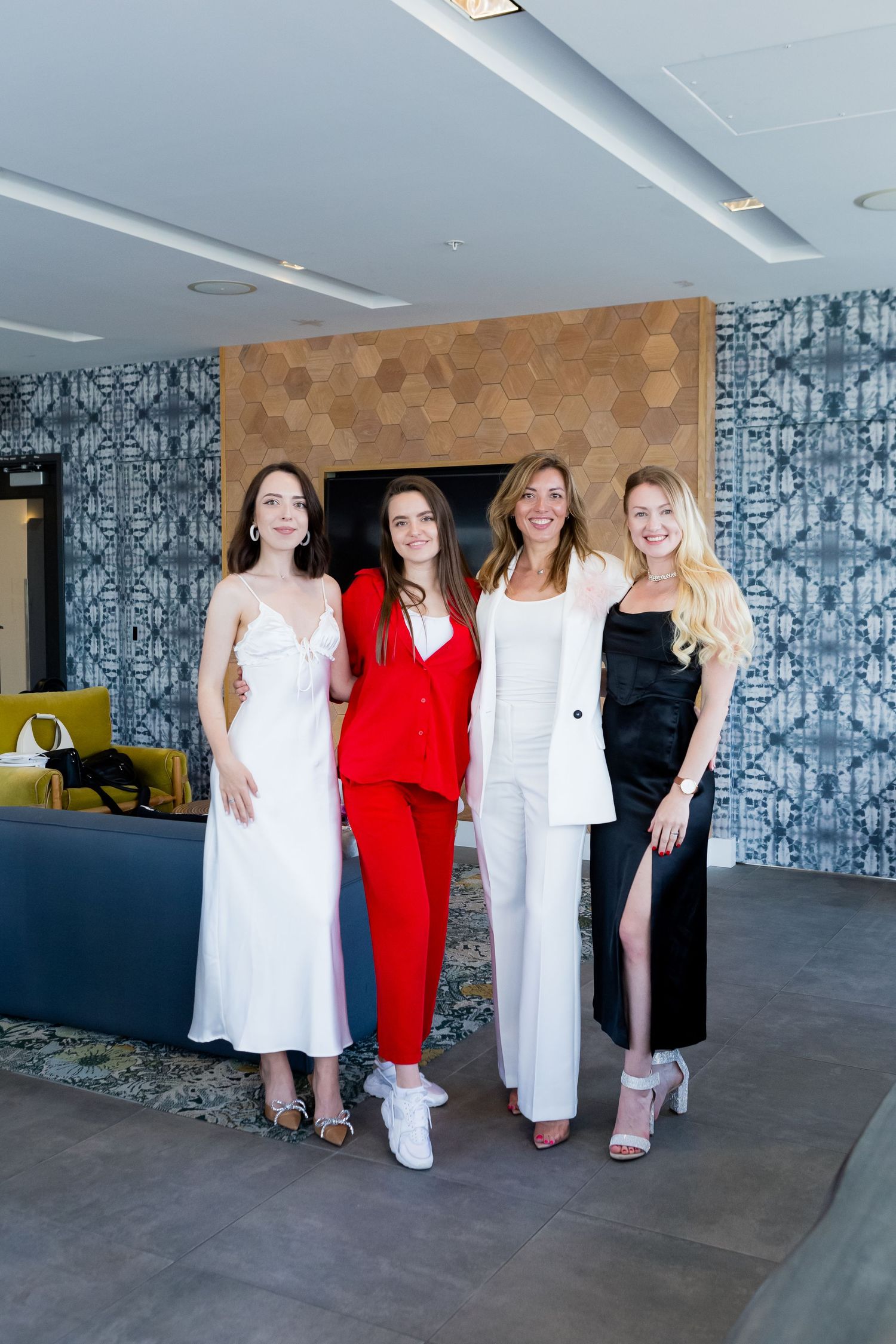 Four people posing in modern space with patterned wallpaper and contemporary furnishings.