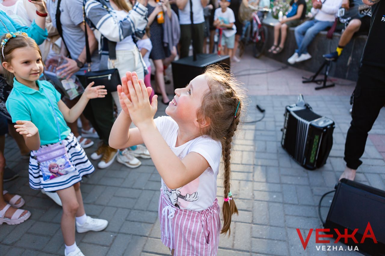 Young children in audience clapping and enjoying outdoor musical performance.