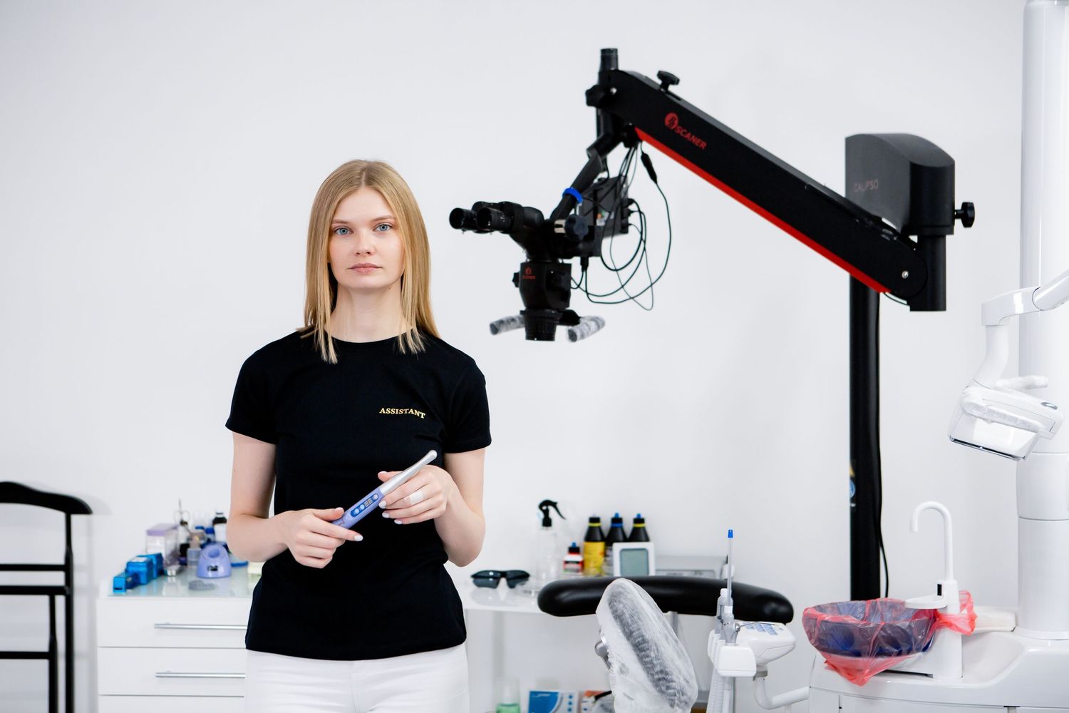 Dental professional in black uniform standing near medical equipment in bright clinic.
