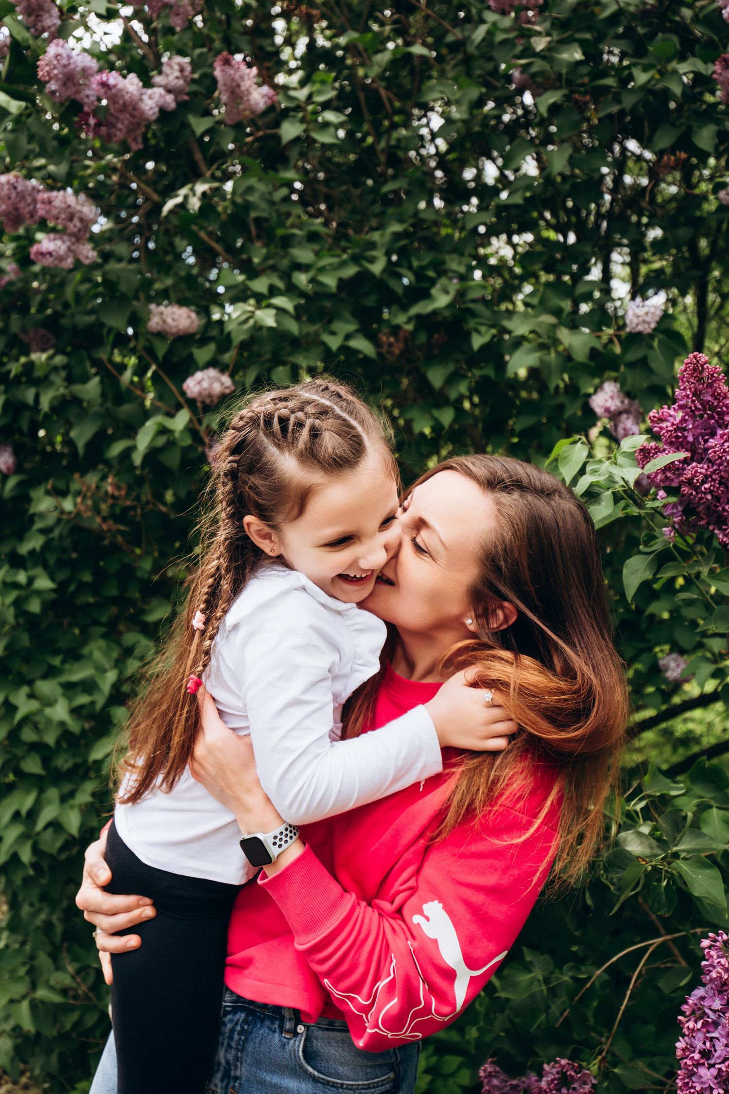 Joyful moment between mother and daughter among blooming lilac bushes.