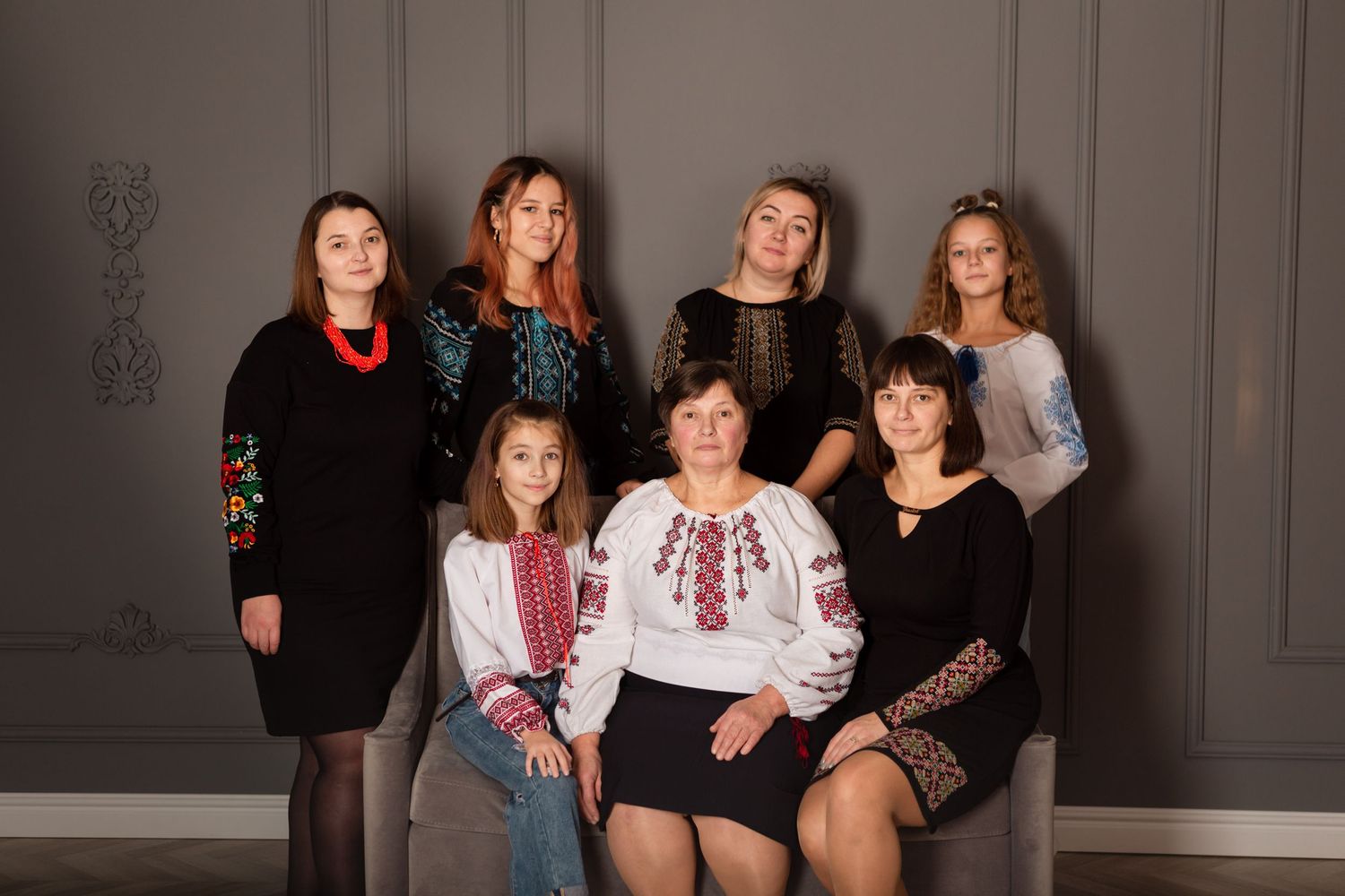 Group portrait of women and girls in festive attire against gray wall.