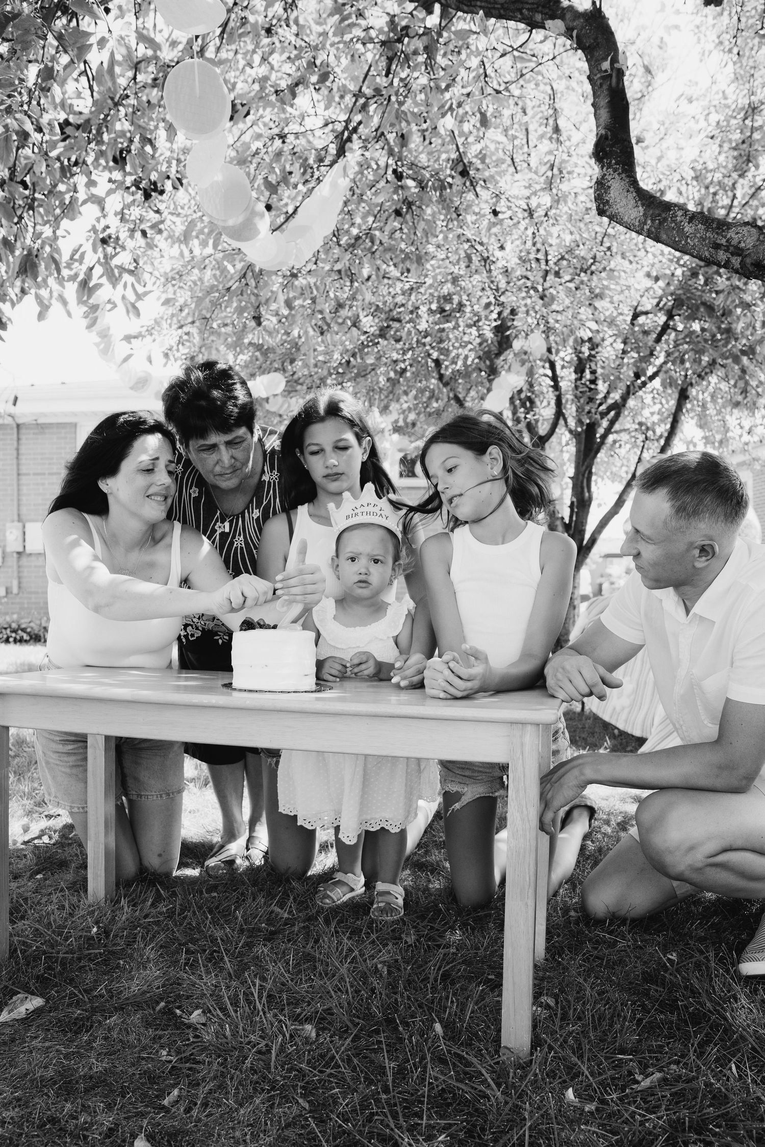 A black and white photo of a celebratory gathering around a table under a tree.