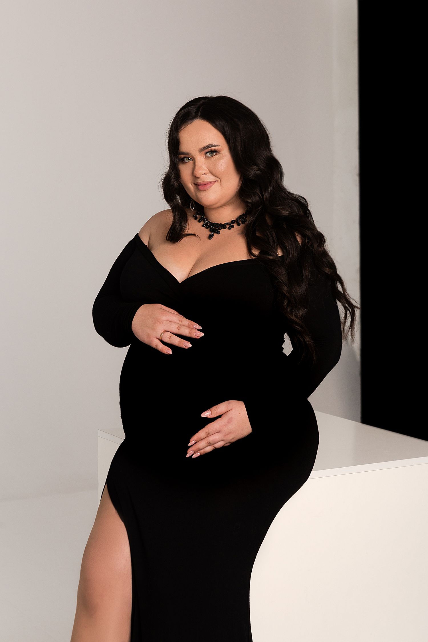 A maternity photo shoot featuring a black formal dress with long sleeves and flowing dark hair.