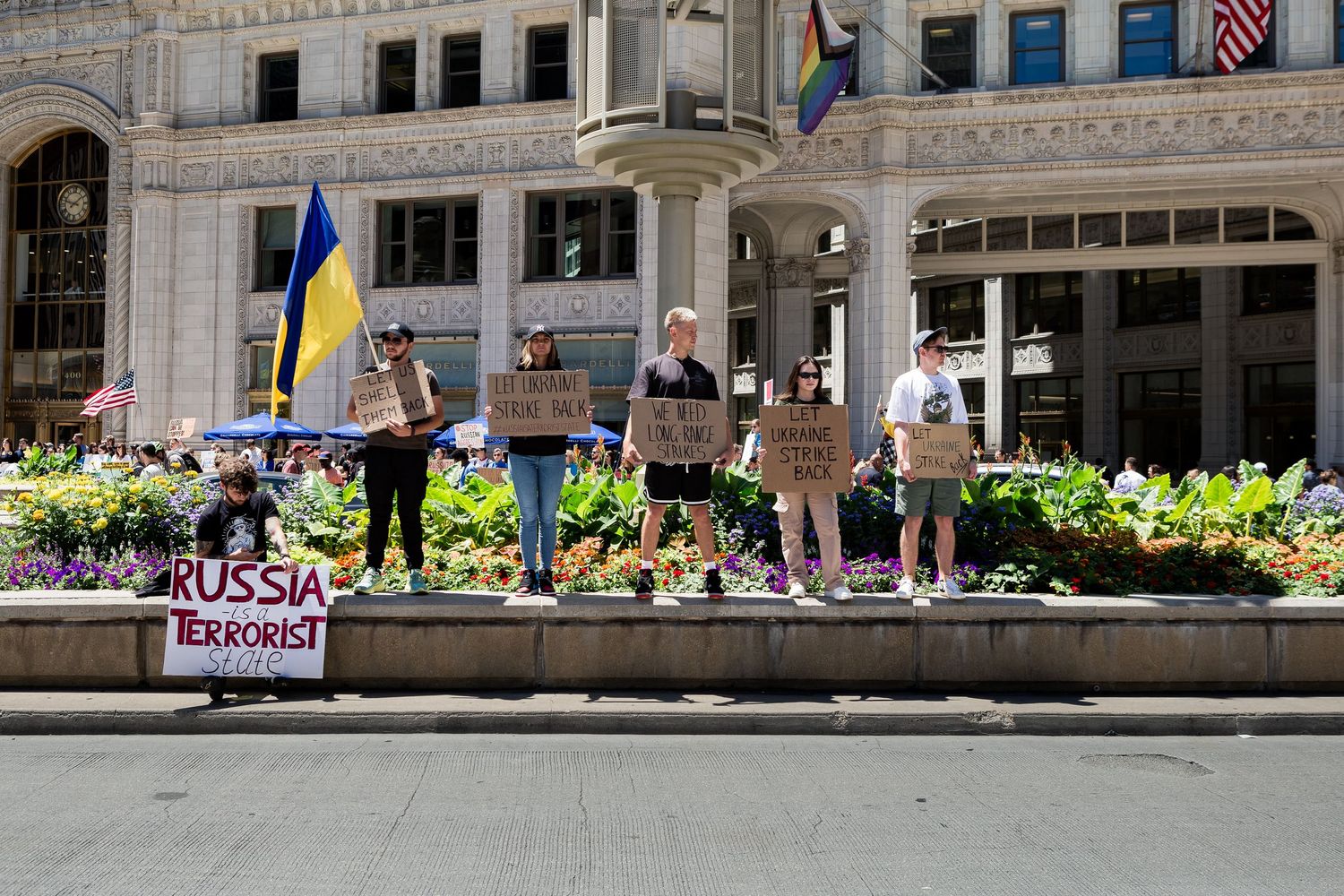 Demonstrators with Ukrainian flags gather on a stone ledge in front of a Chicago building.