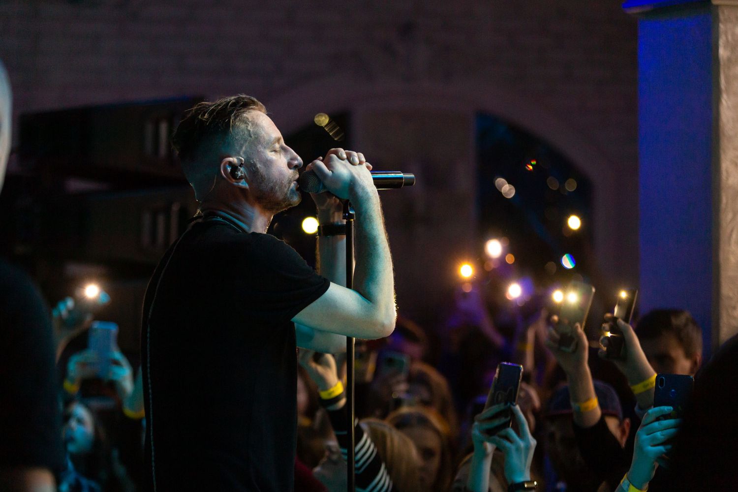 A performer sings on stage with an energetic crowd visible in the background.