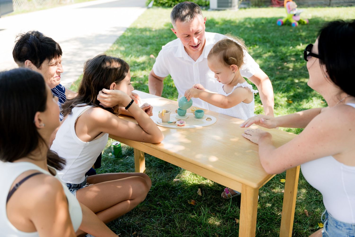 A group gathers around a wooden table for an outdoor celebration with refreshments.