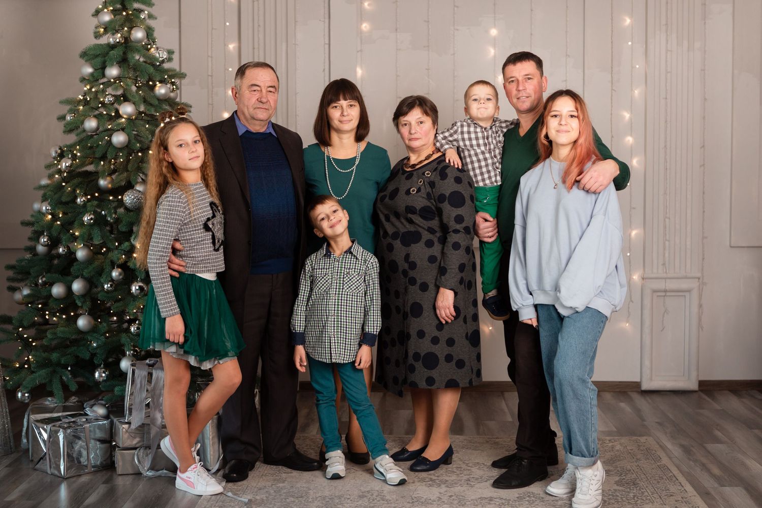 Family gathering in casual winter outfits by decorated Christmas tree with twinkling lights.