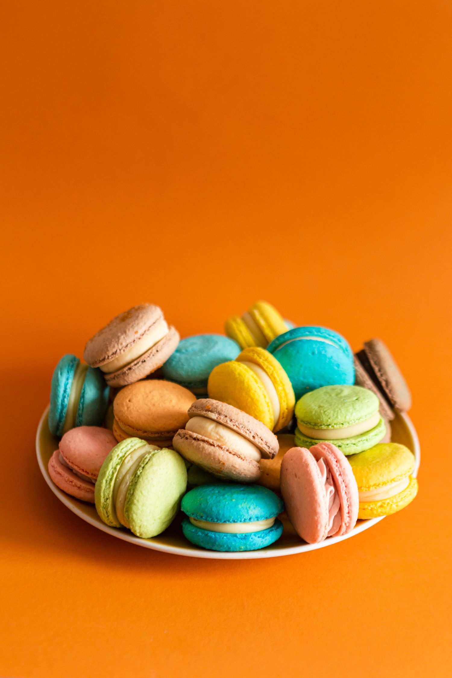 Plate of colorful French macarons in pastel shades against vibrant orange background.