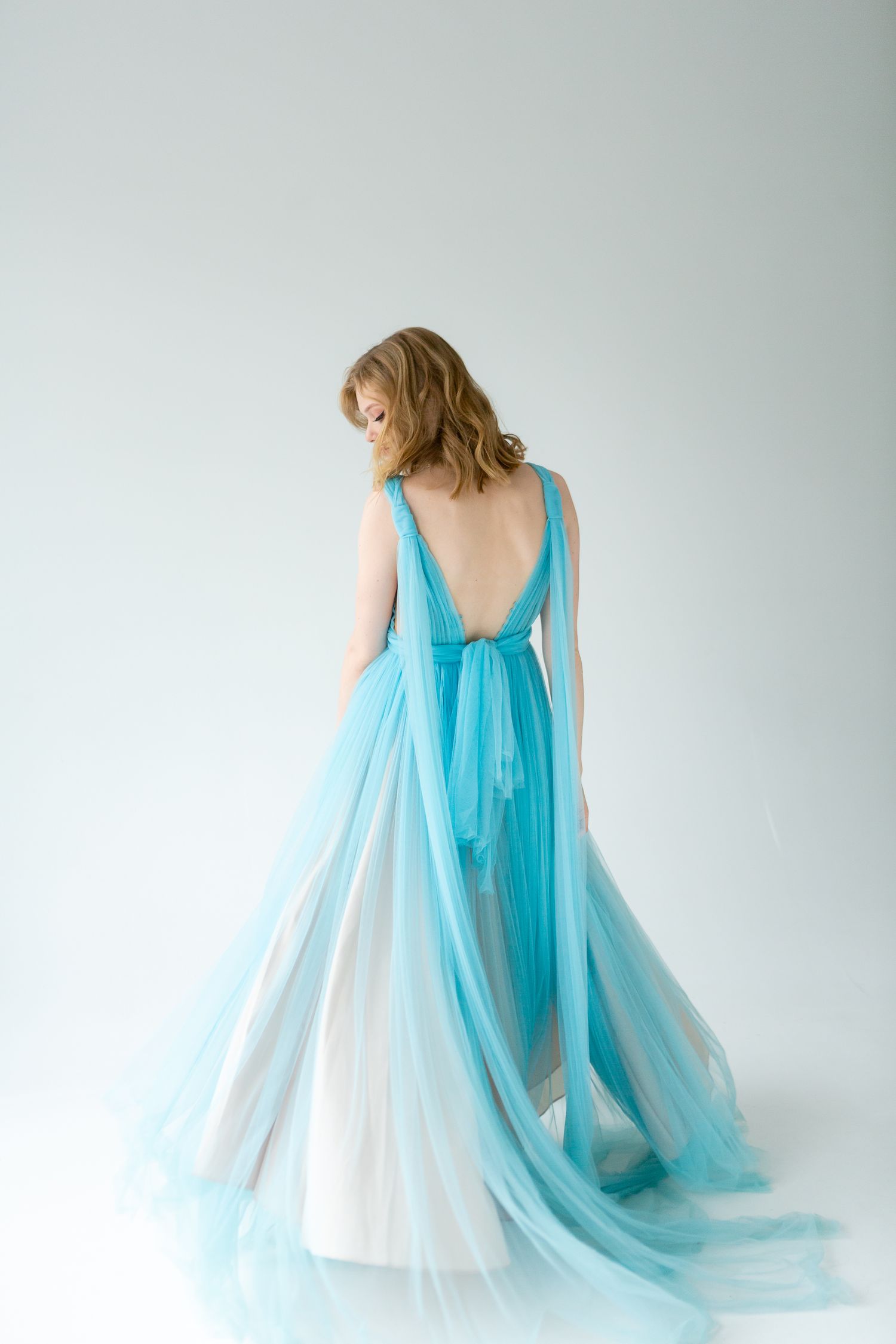 Back view of elegant turquoise ombre gown with deep V back against white background.