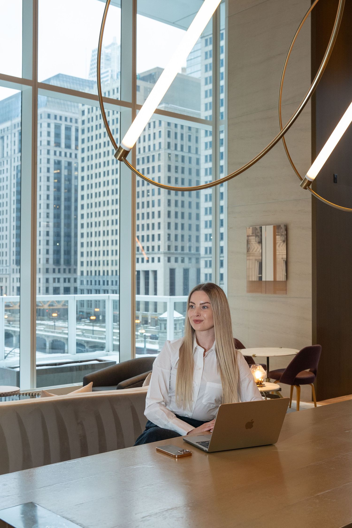 Professional working on laptop in modern office lounge with city backdrop.