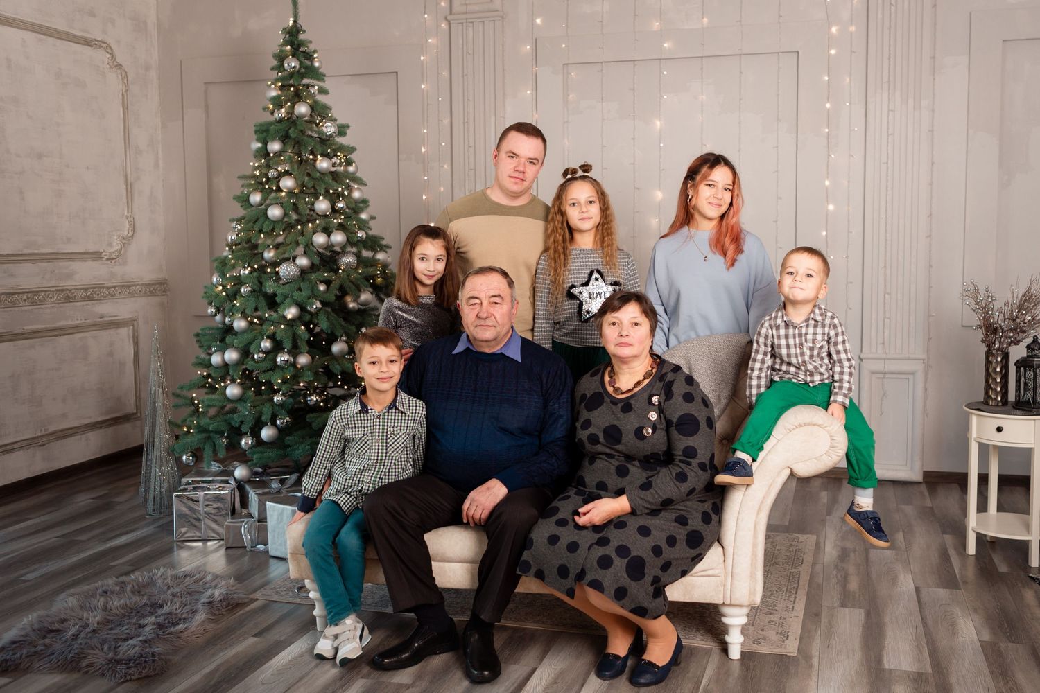 Multi-generational family portrait with Christmas tree in elegant grey studio setting.
