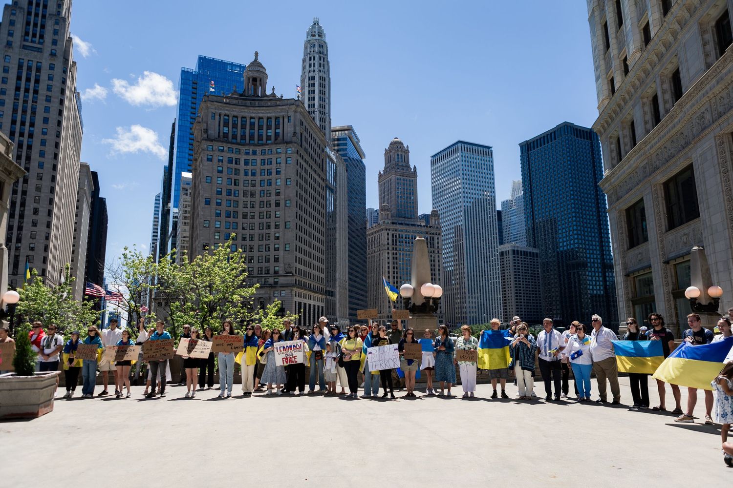 A line of protesters with Ukrainian flags and signs spreads across a Chicago street with tall buildings behind.