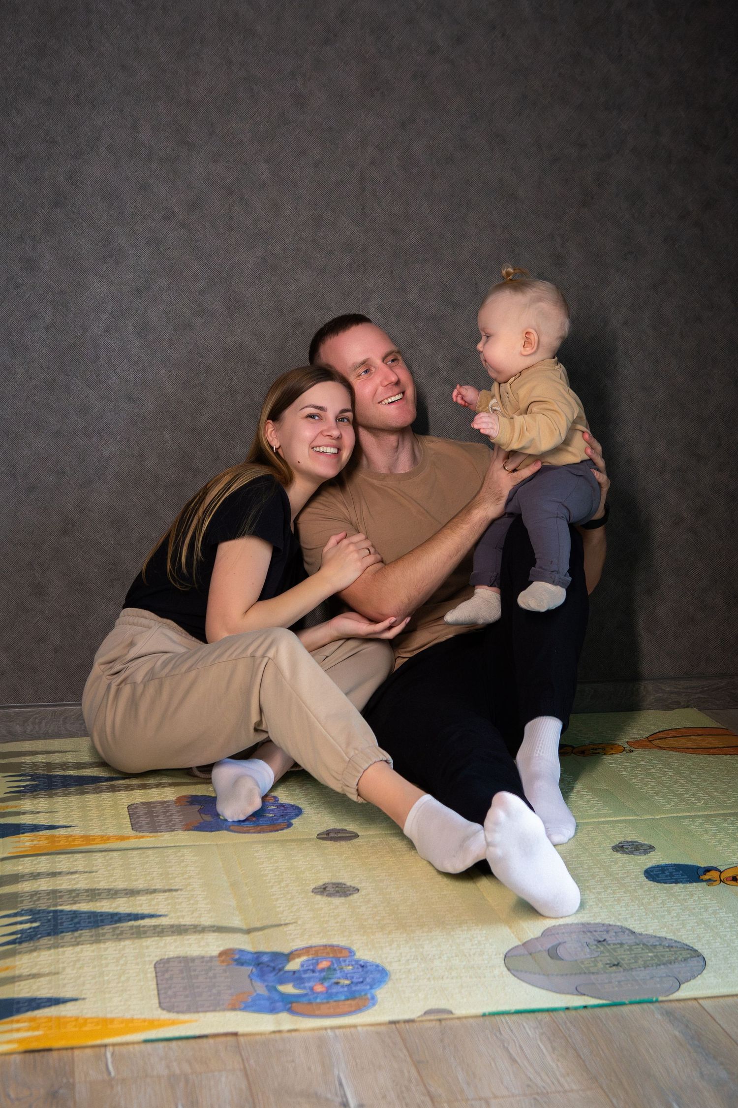 A sequence of playful family moments shown in five connected photos on a patterned mat or blanket.