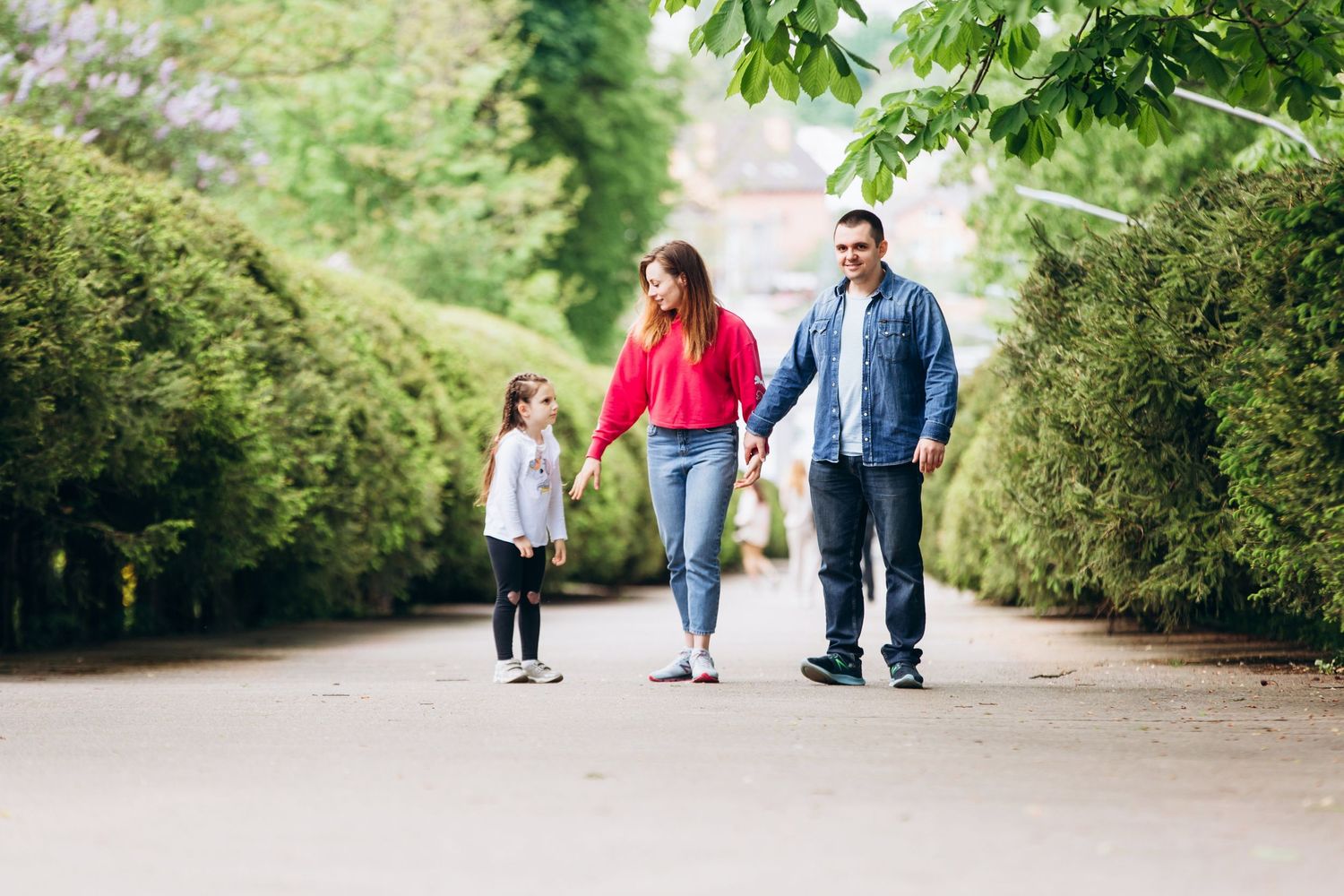 Three people walking together on a tree-lined path on a sunny day.