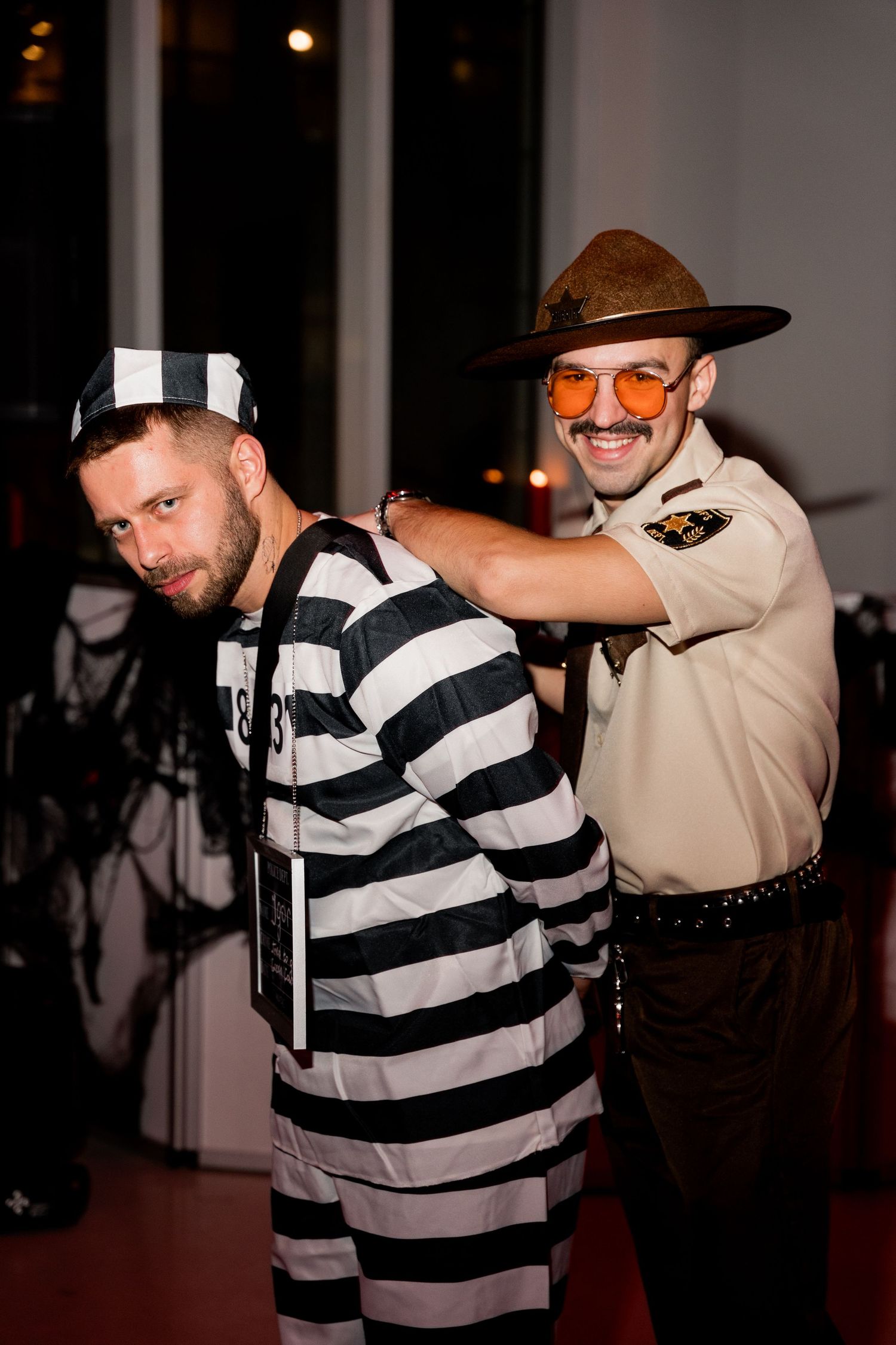 Person in prisoner costume being apprehended by someone dressed as a police officer at a costume party.