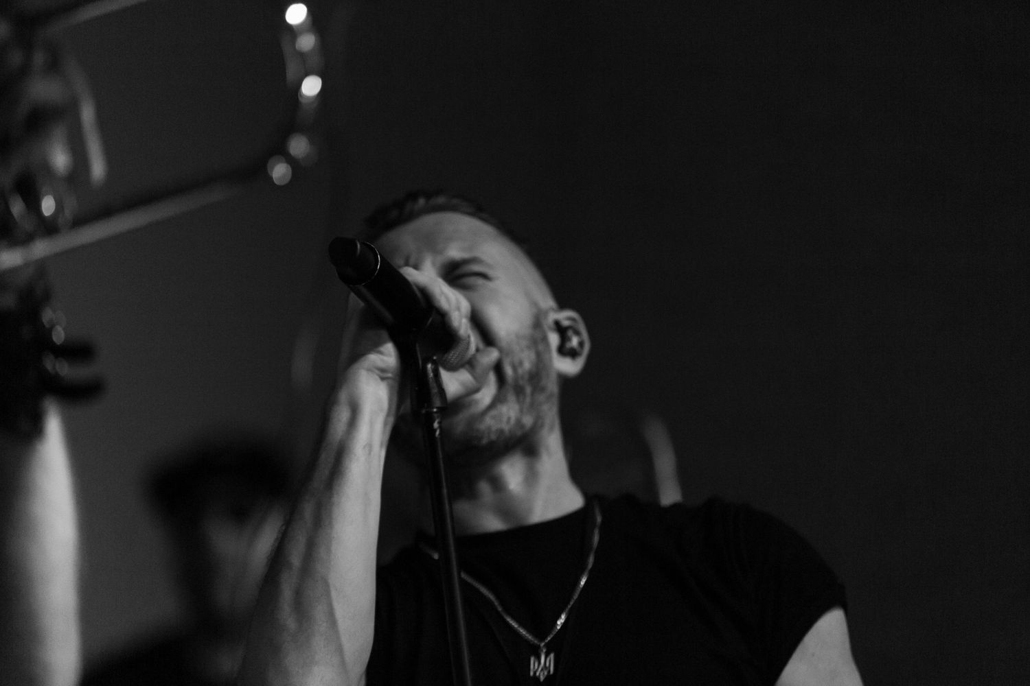 Black and white dramatic shot of performer singing passionately into microphone during concert.