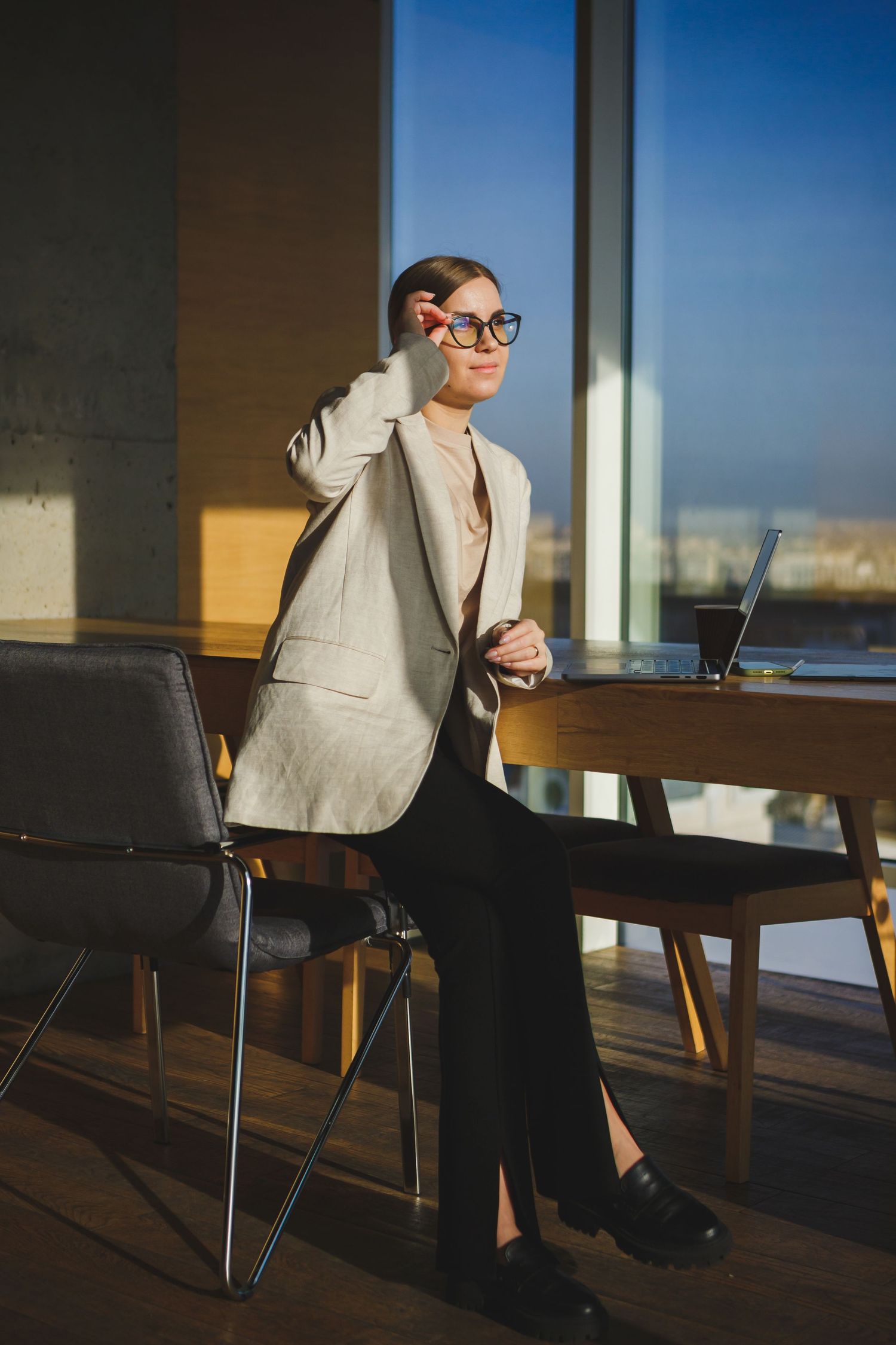 Professional in gray suit talking on phone while standing at office desk.
