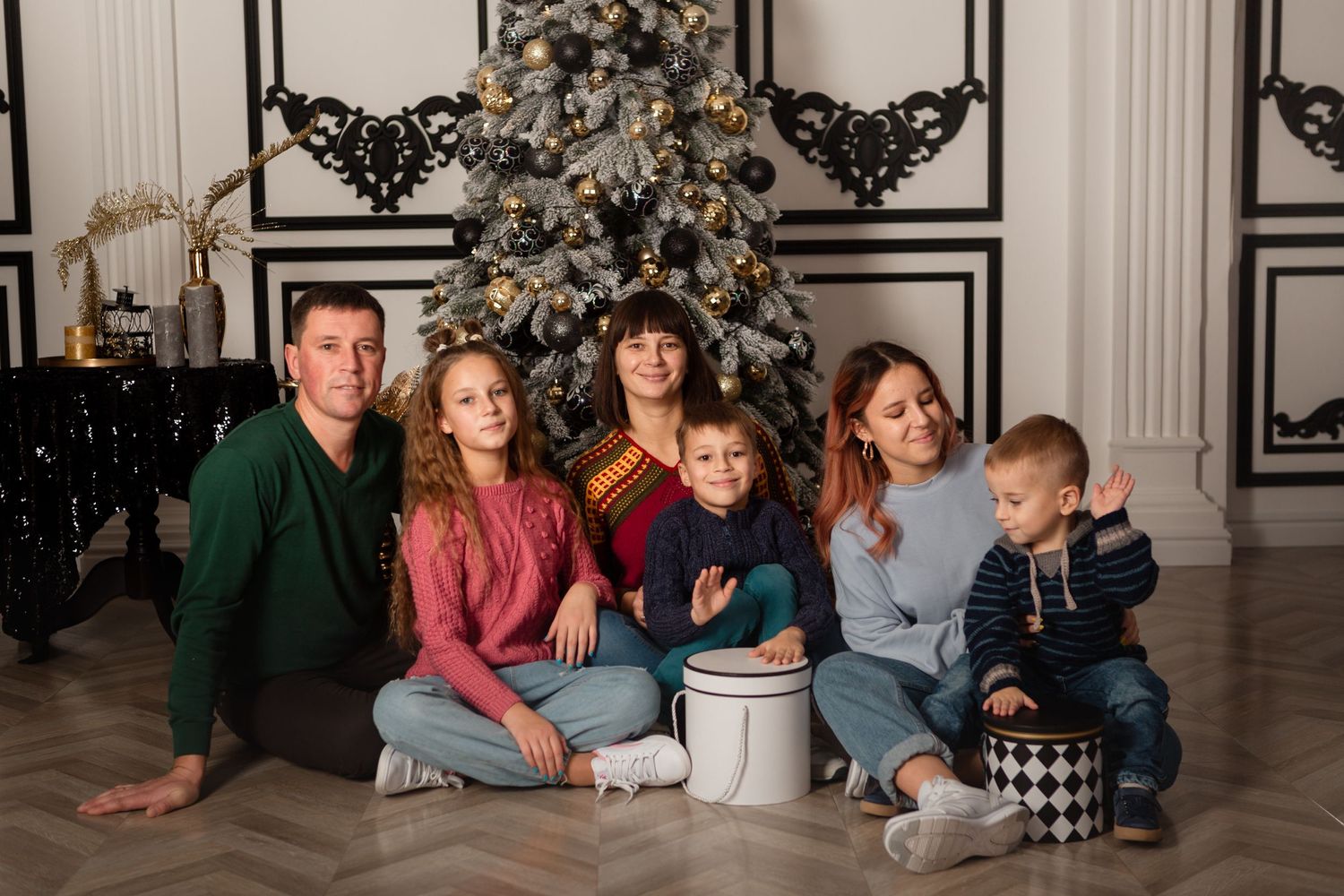 Family holiday portrait with decorated tree and white paneled walls in background.