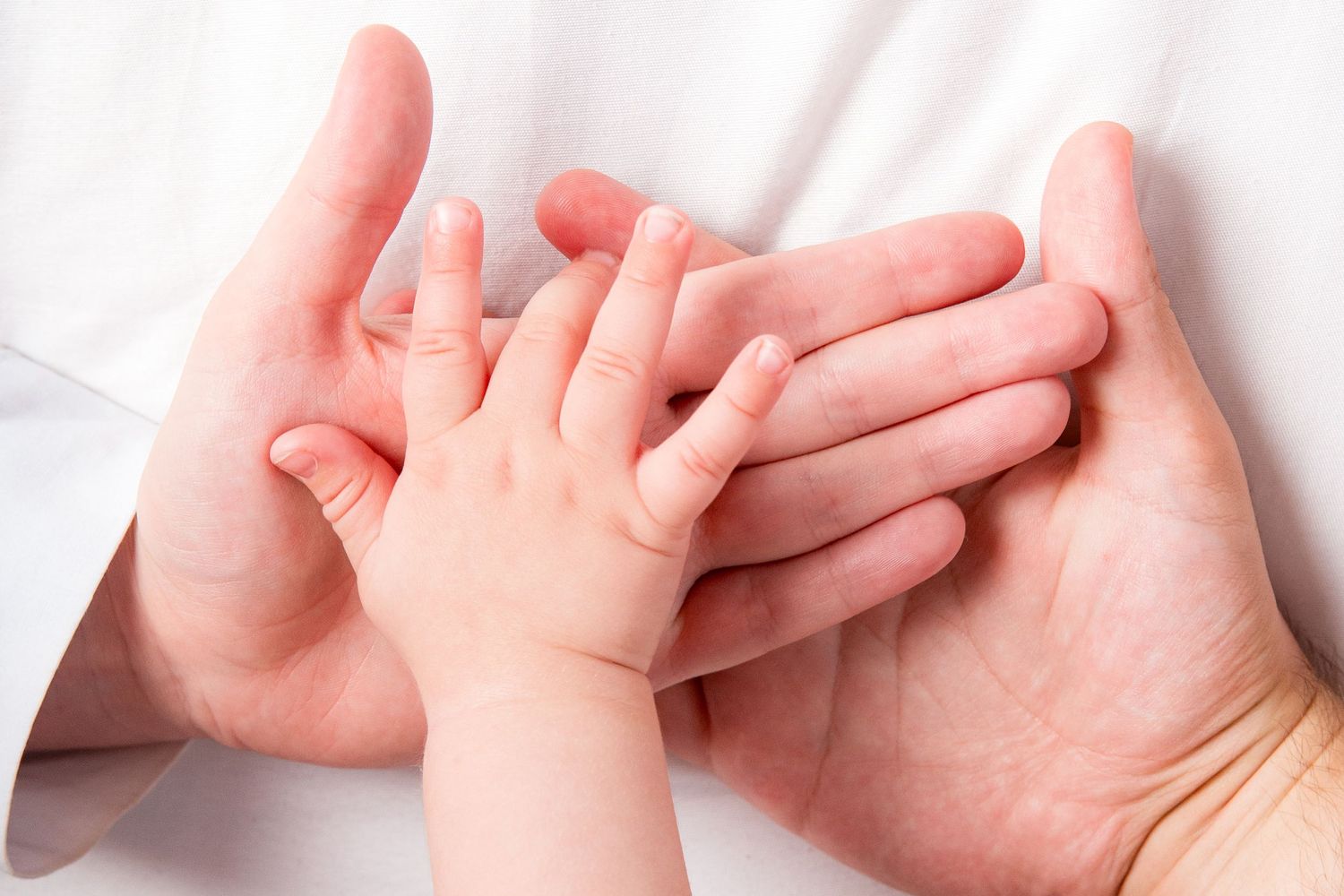 Close up of baby's tiny hand grasping adult fingers against white background.