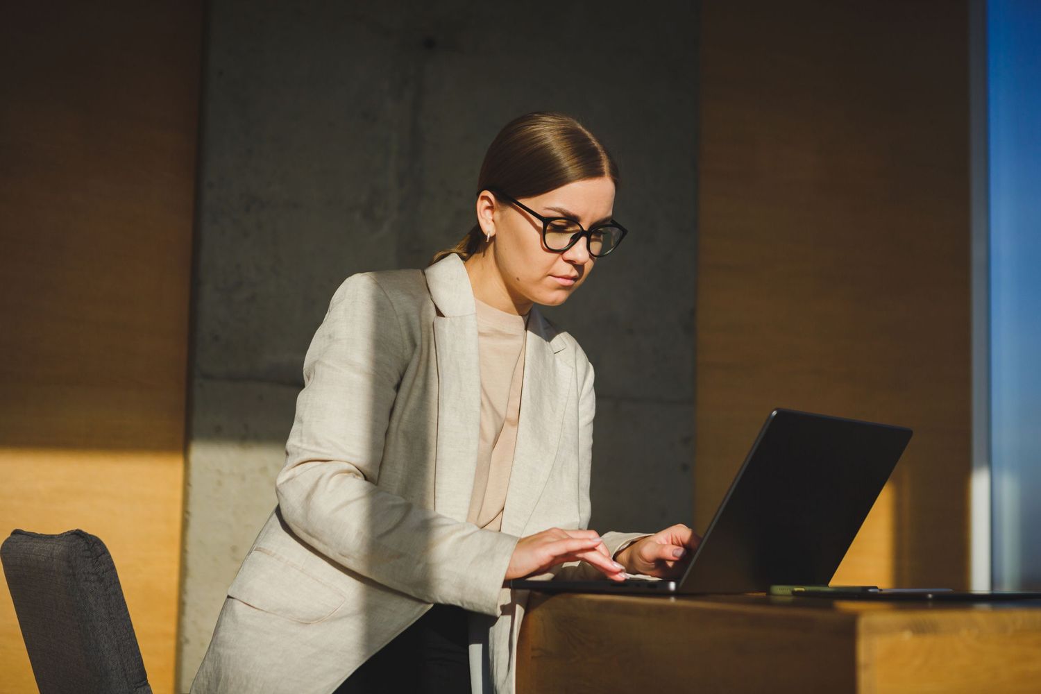 Business professional in gray blazer working on laptop at modern office desk.