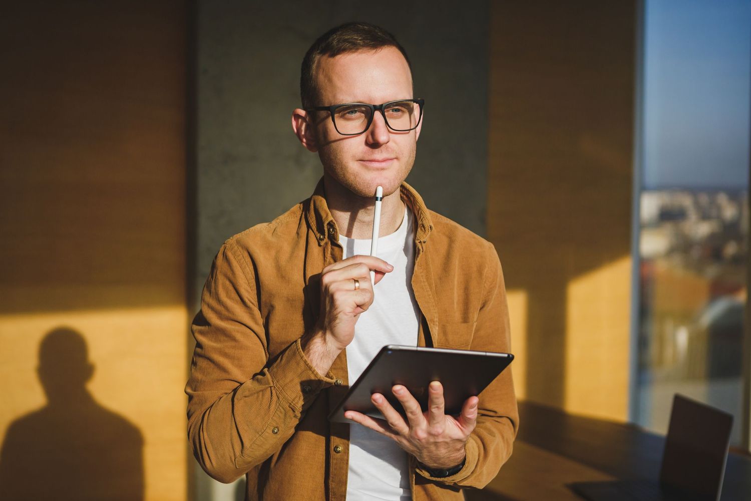 Professional holding tablet and pen while working in sunlit modern office space.