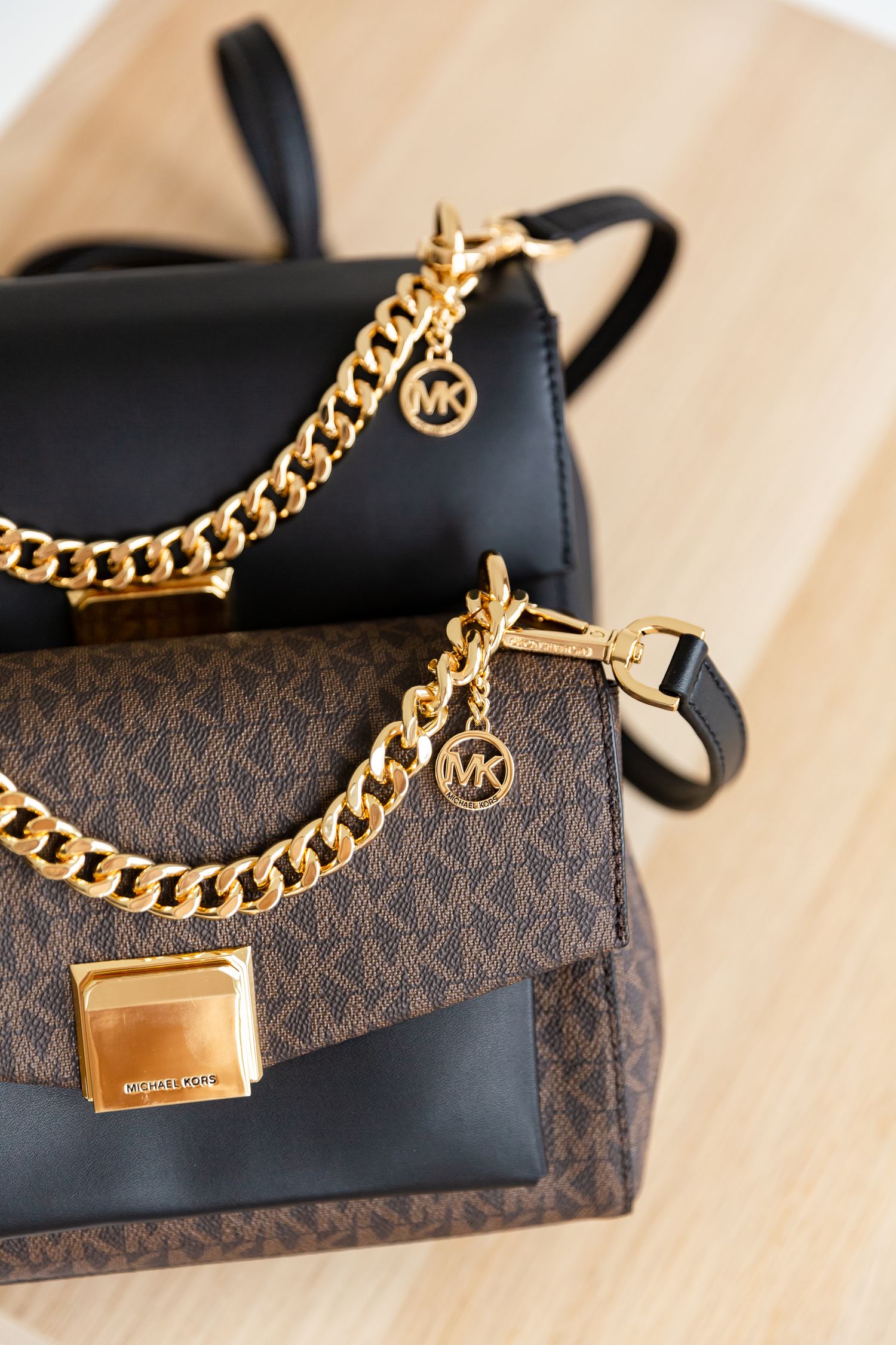 Michael Kors monogram bags with gold chain details and MK charms displayed on wooden surface.