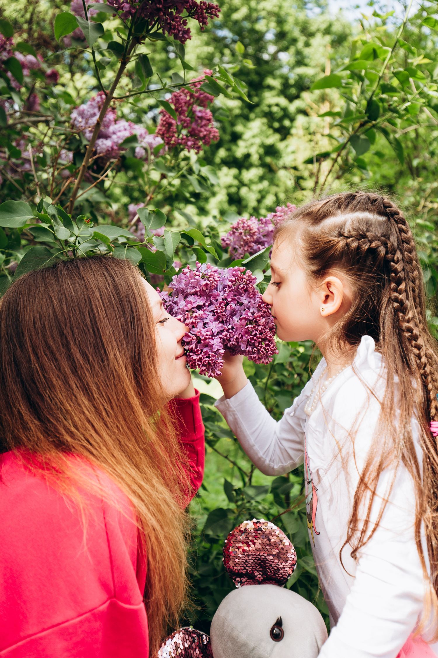 Mother and daughter smelling purple lilac blooms in spring garden.