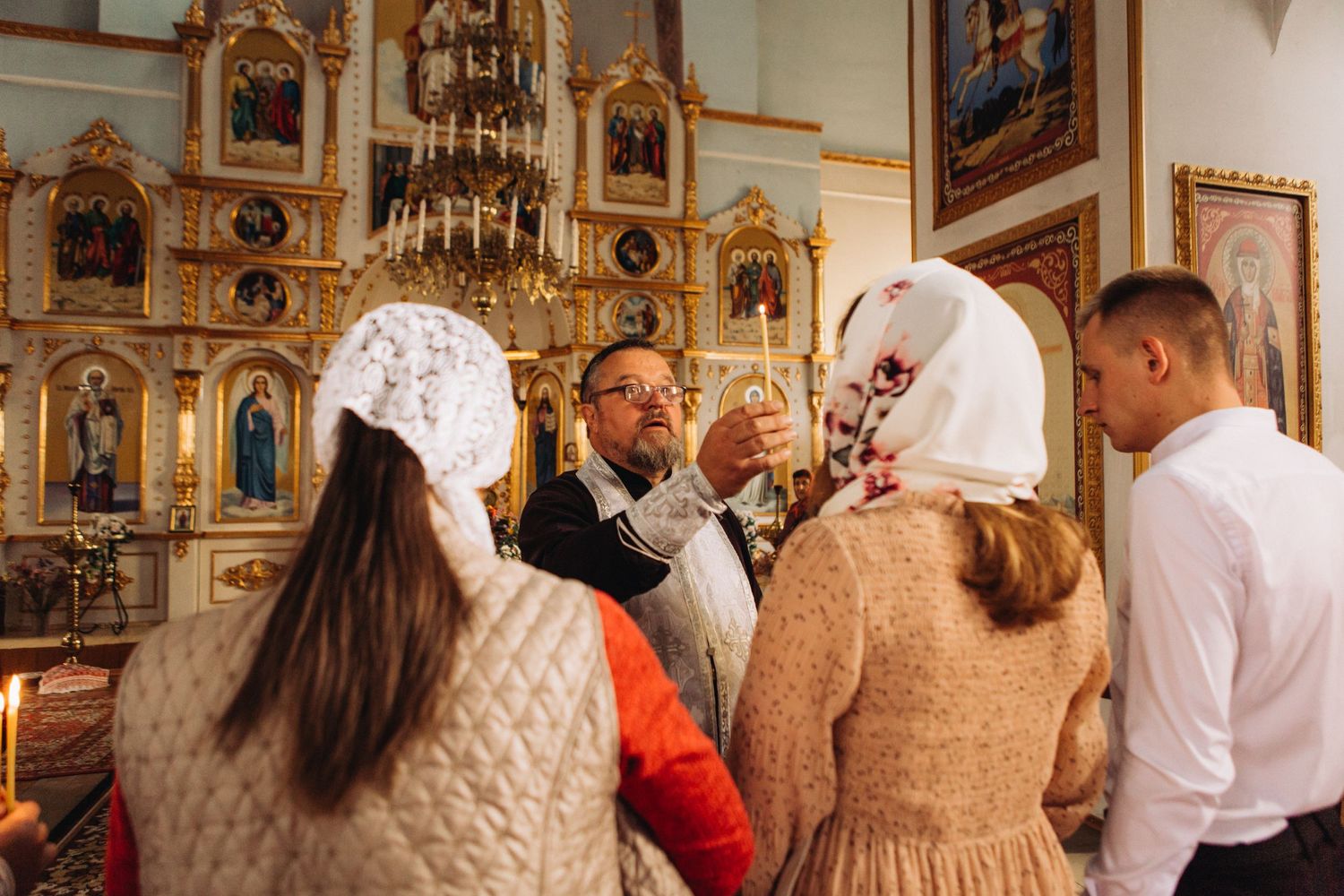 A baptism ceremony taking place inside a traditional orthodox church with gilded iconostasis.