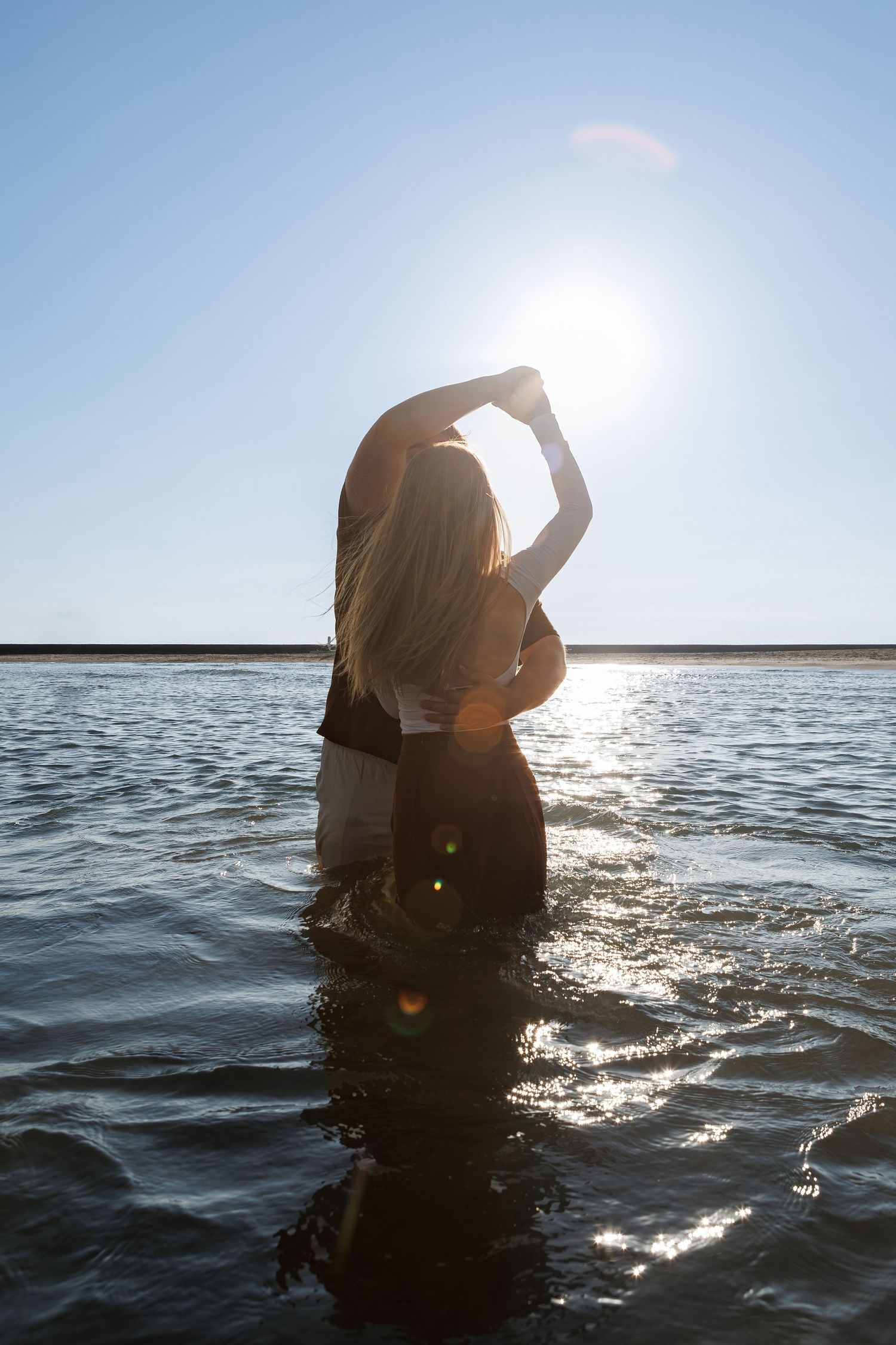 Silhouette of person standing in ocean water during sunset creating sparkling reflections on rippling waves.