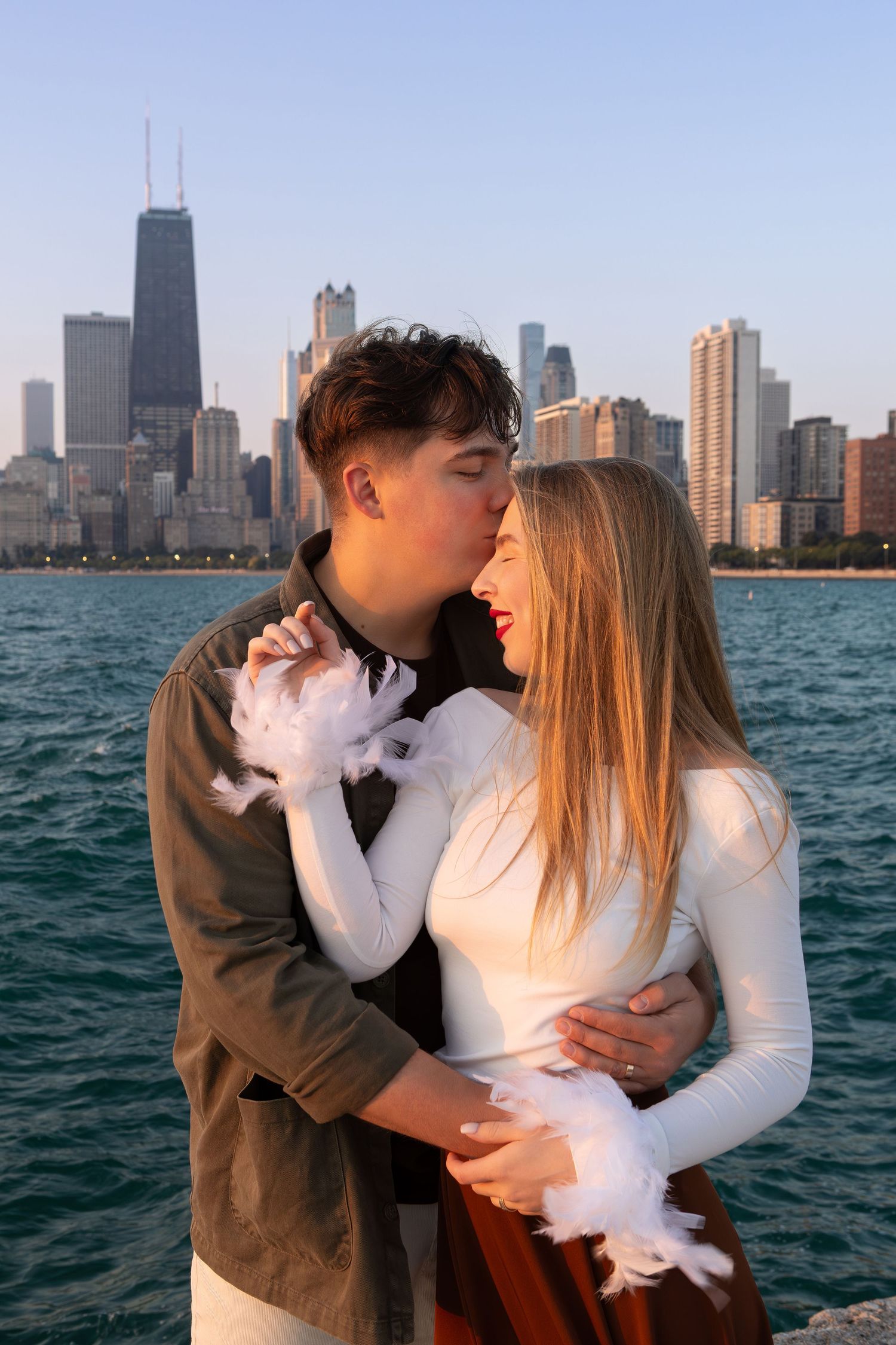 A couple shares romantic moments along Lake Michigan with the Chicago skyline in the background at sunset.