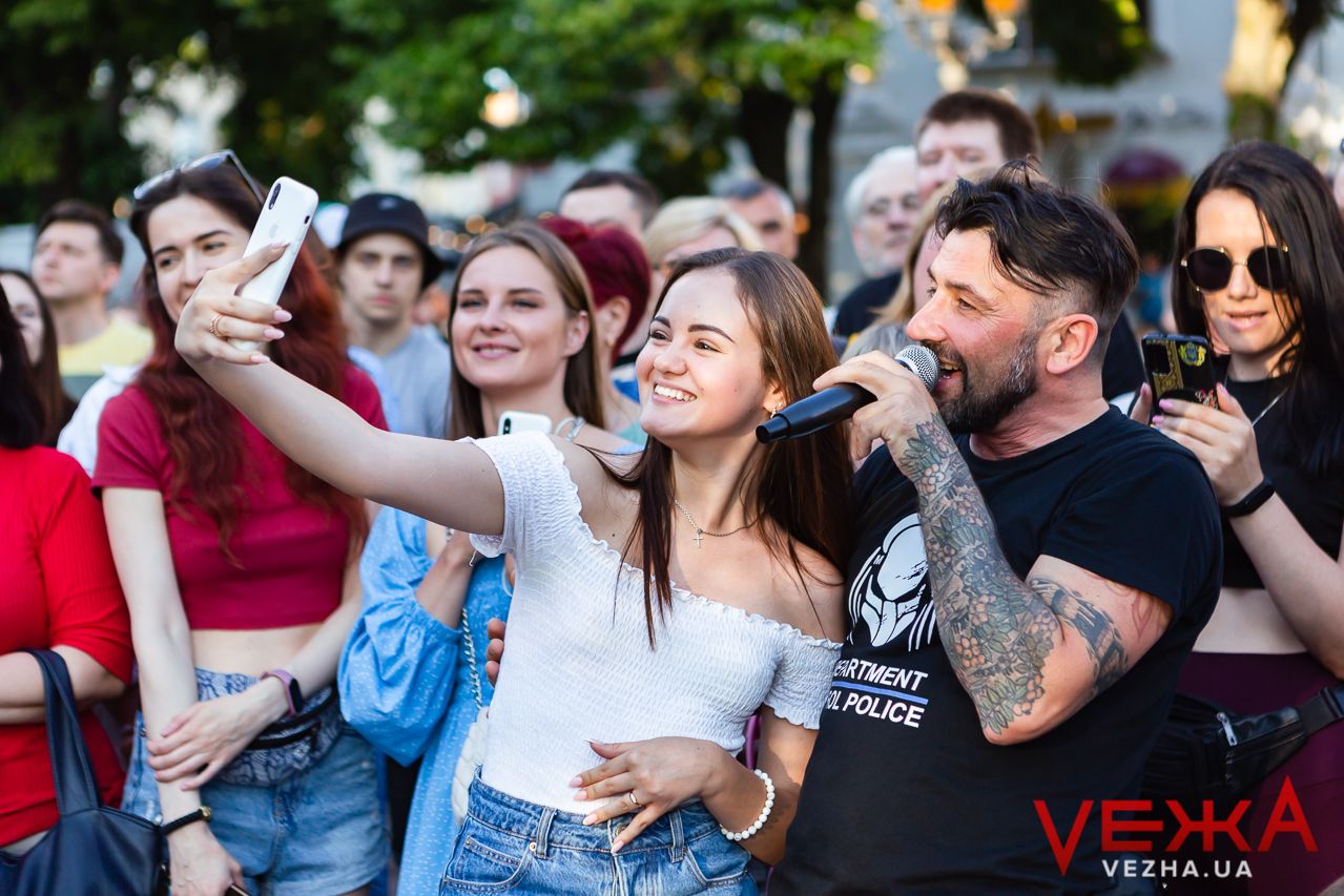 Concert attendees taking selfies while enjoying outdoor music performance.